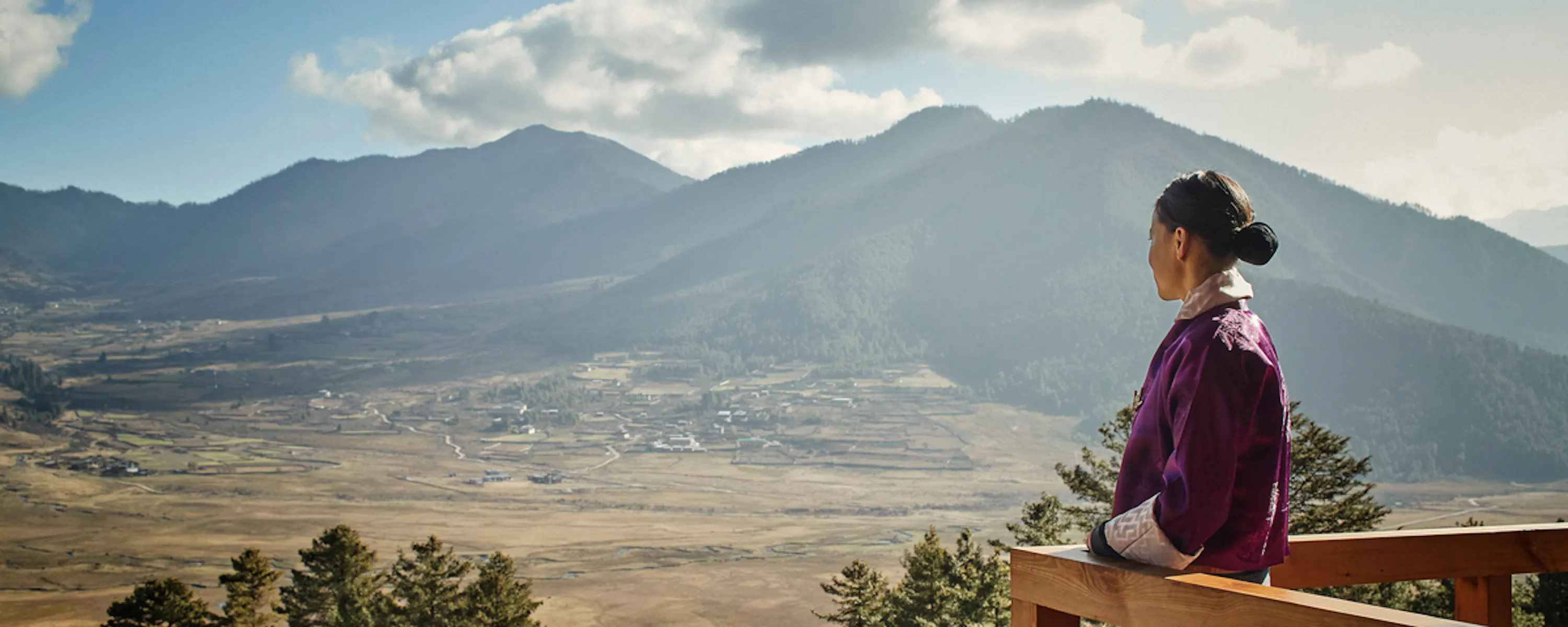 A host looks out over the wide Phobjikha Valley from Six Senses Gangtey, framed by terrace and mountains.