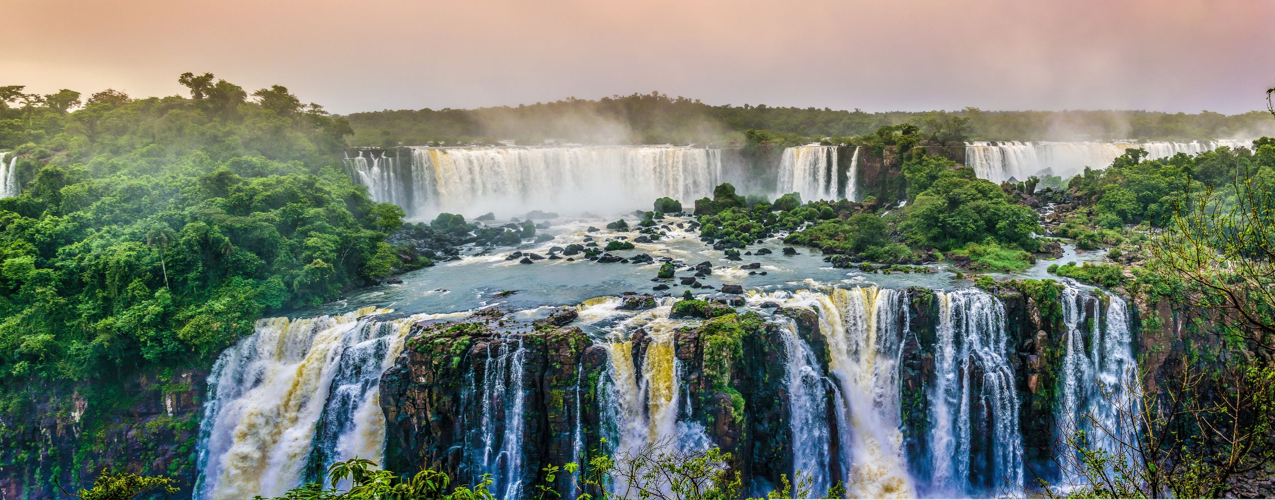 Powerful white cascades thunder through dense green forest at Iguacu Falls, viewed from above the deep gorge below.