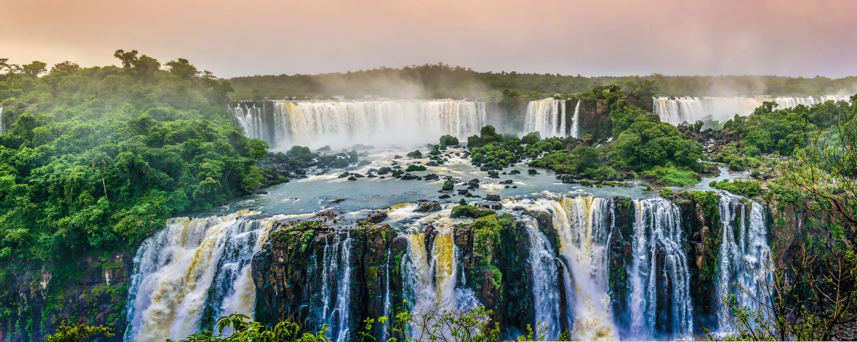 Powerful white cascades thunder through dense green forest at Iguacu Falls, viewed from above the deep gorge below.