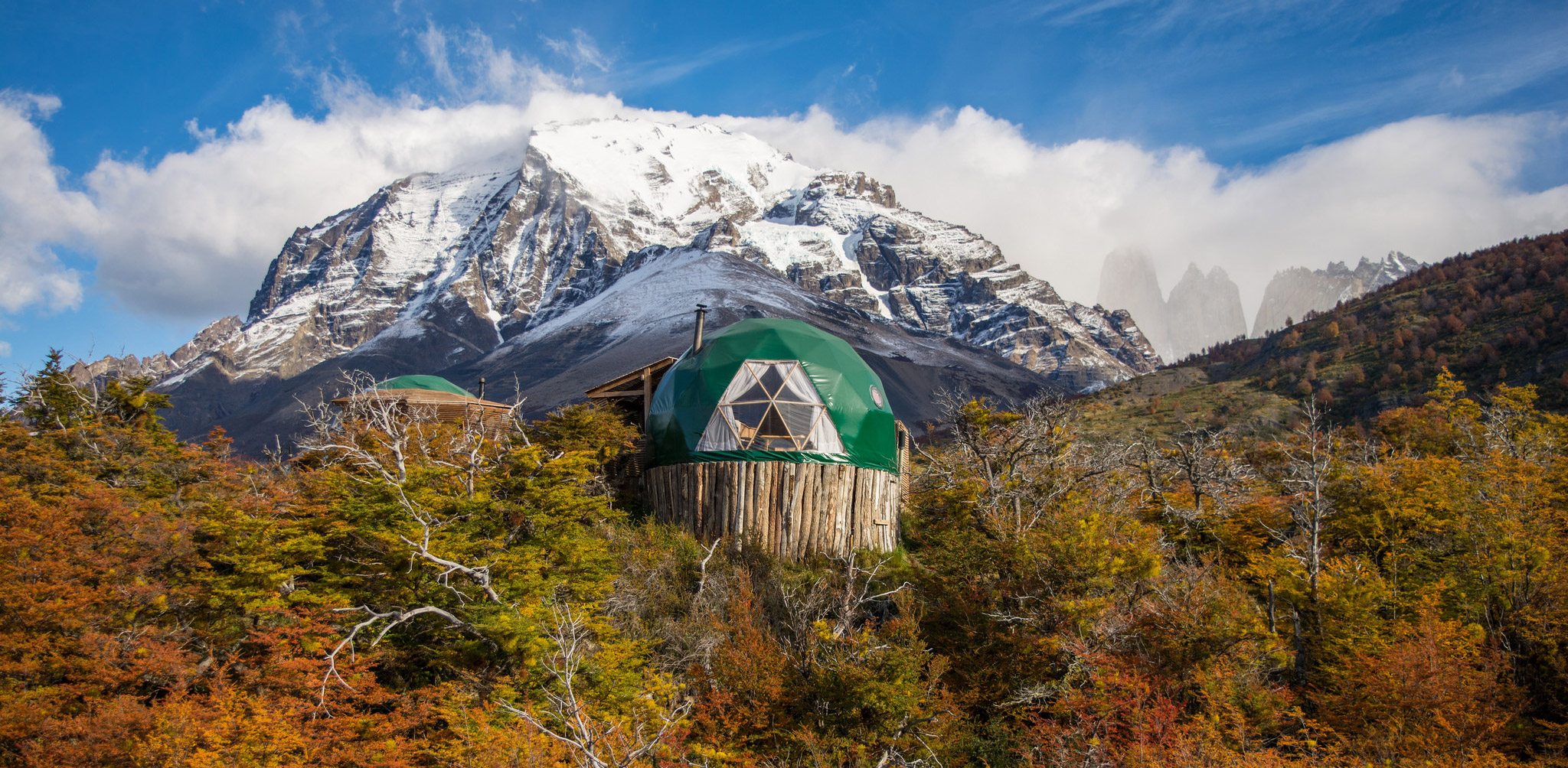 A green dome camp beneath snowy peaks and autumn brush at EcoCamp Patagonia, set in Chile's Torres del Paine.