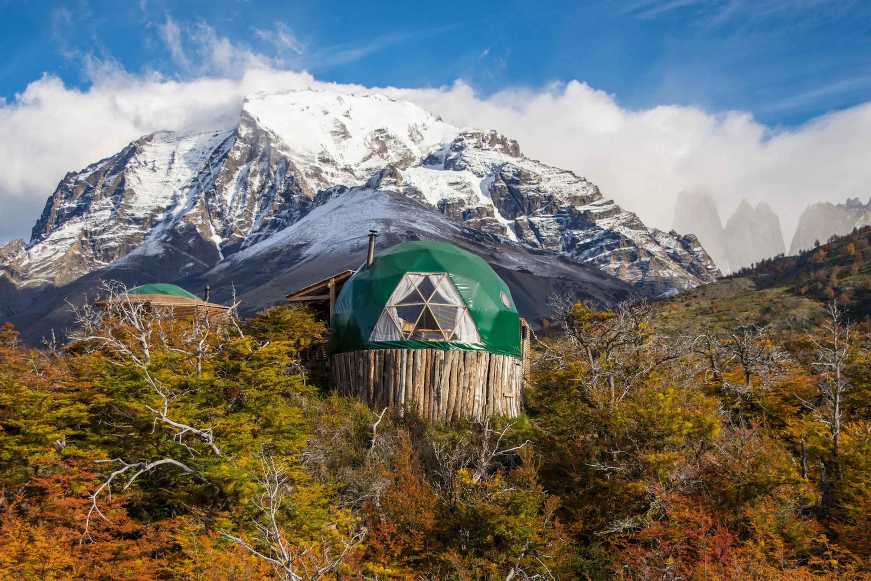 A green dome camp beneath snowy peaks and autumn brush at EcoCamp Patagonia, set in Chile's Torres del Paine.