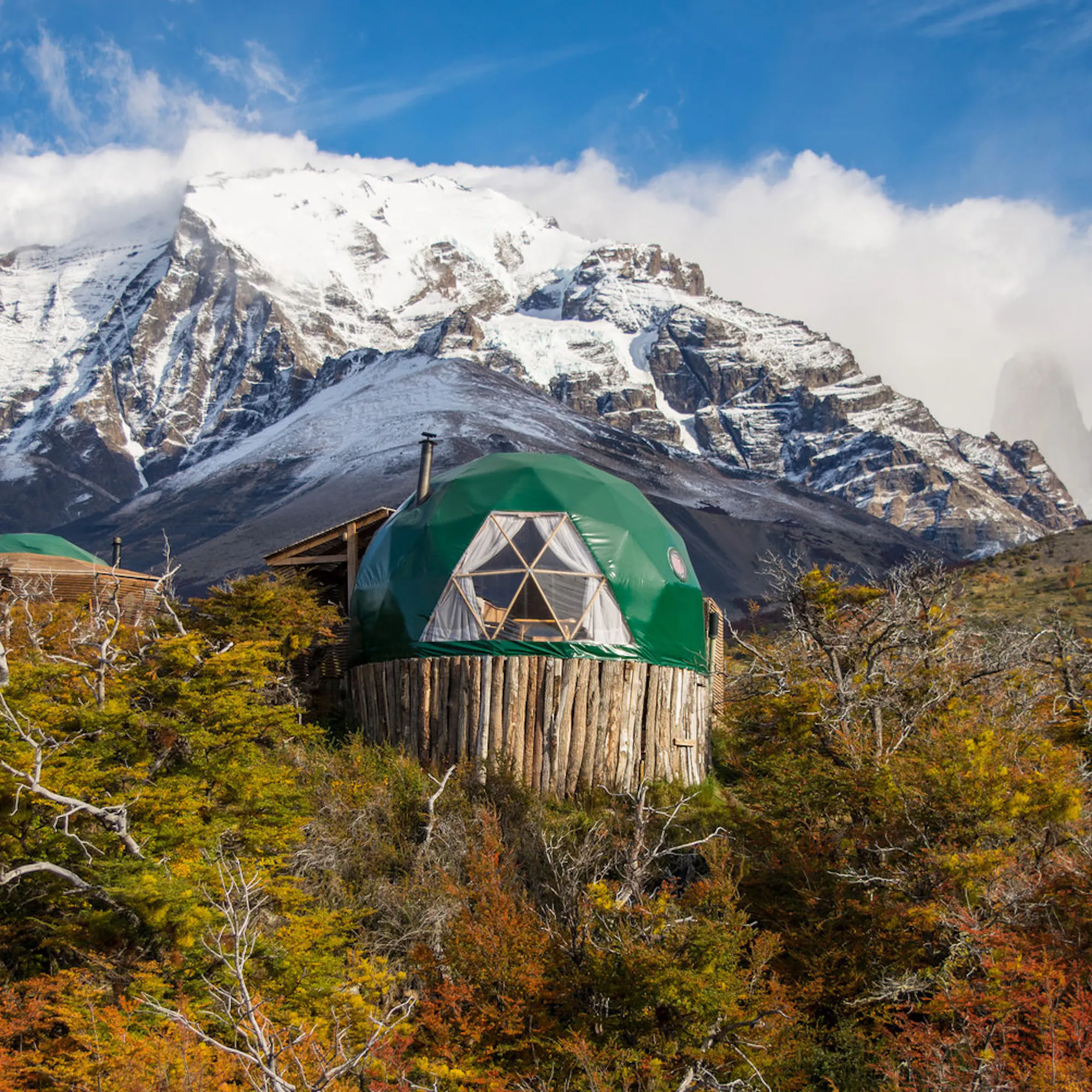 A green dome camp beneath snowy peaks and autumn brush at EcoCamp Patagonia, set in Chile's Torres del Paine.