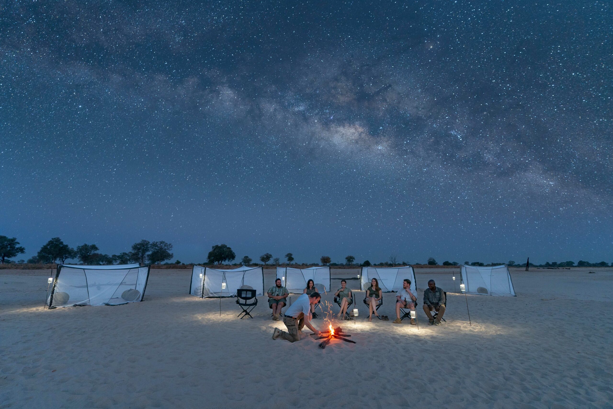 A sleepout camp sits beneath the Milky Way on a sandy plain in Zambia's South Luangwa, with tents below the sky.