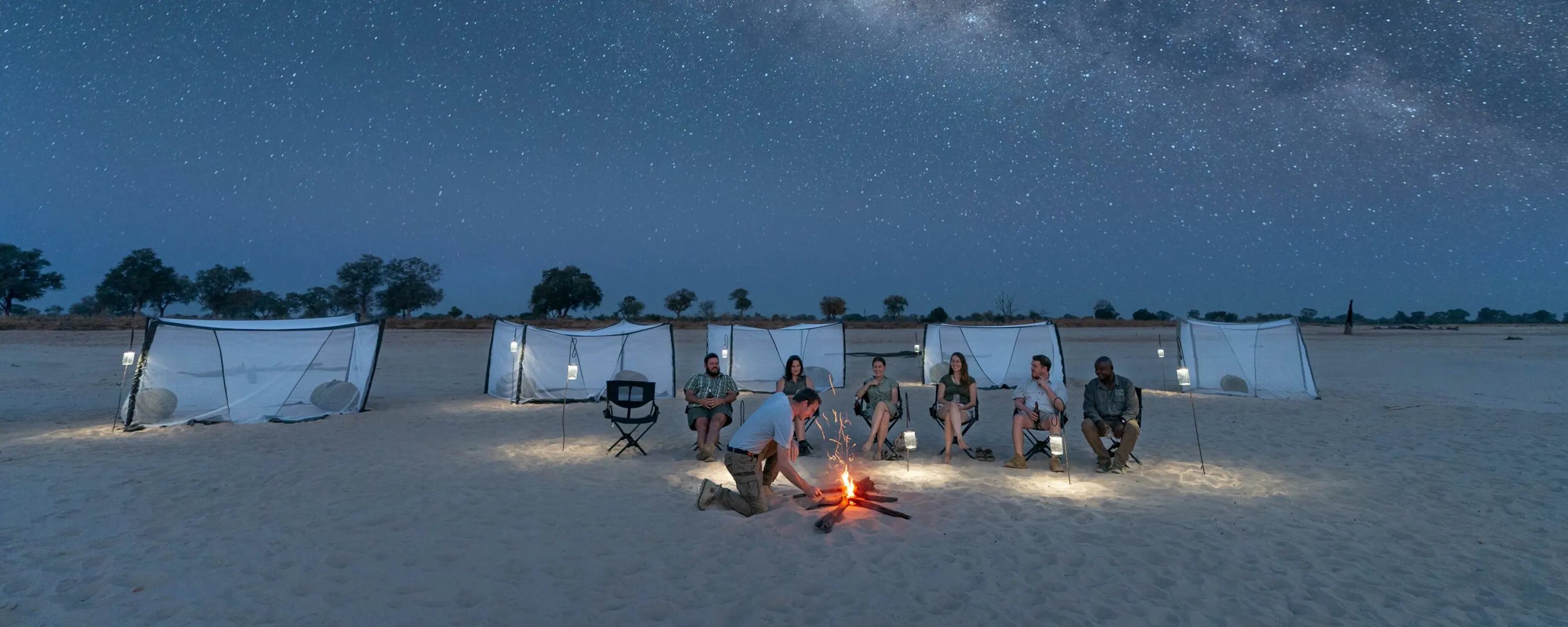 A sleepout camp sits beneath the Milky Way on a sandy plain in Zambia's South Luangwa, with tents below the sky.