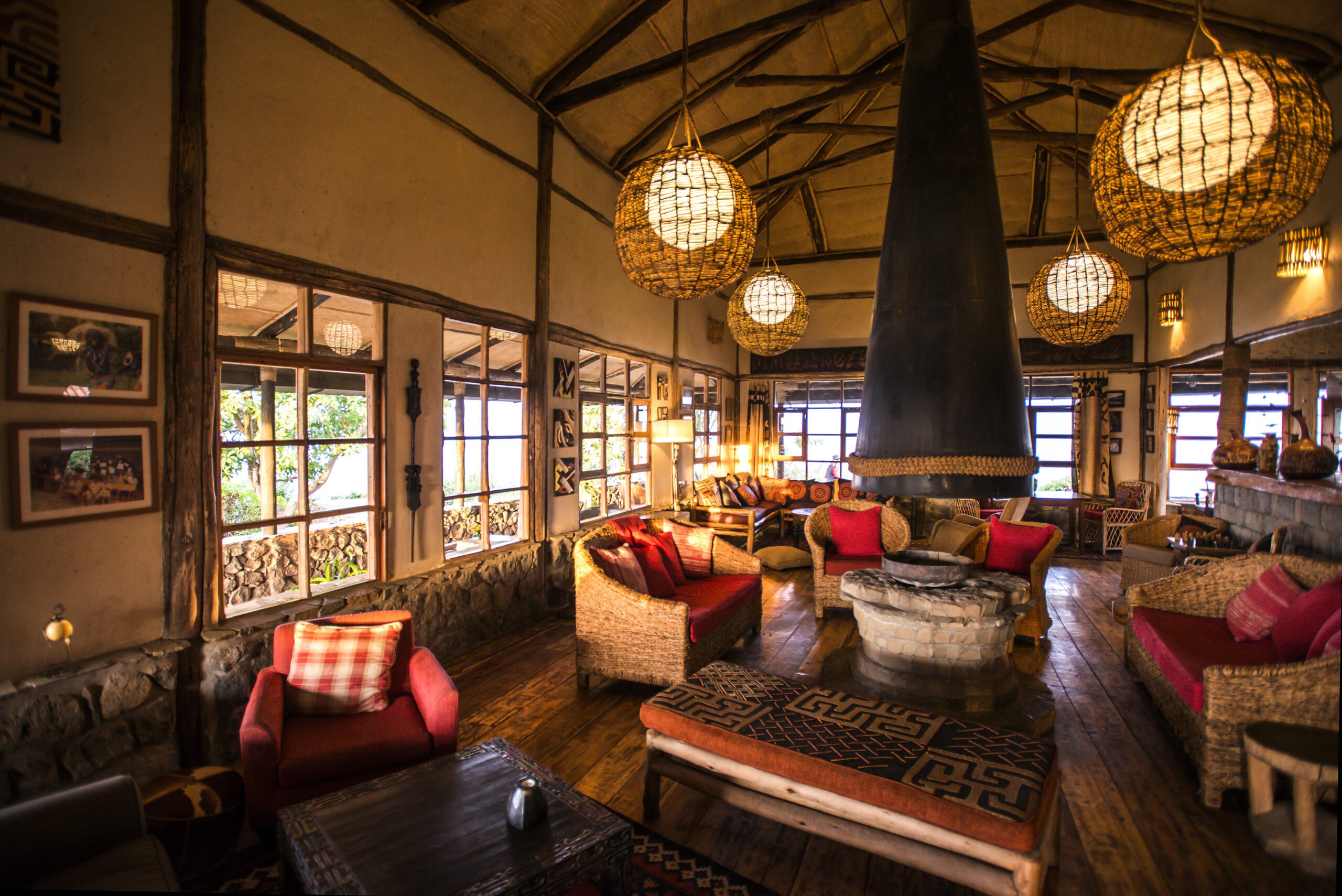 Warm lantern light fills the lounge at Virunga Lodge, with woven chairs, timber beams, and broad windows.