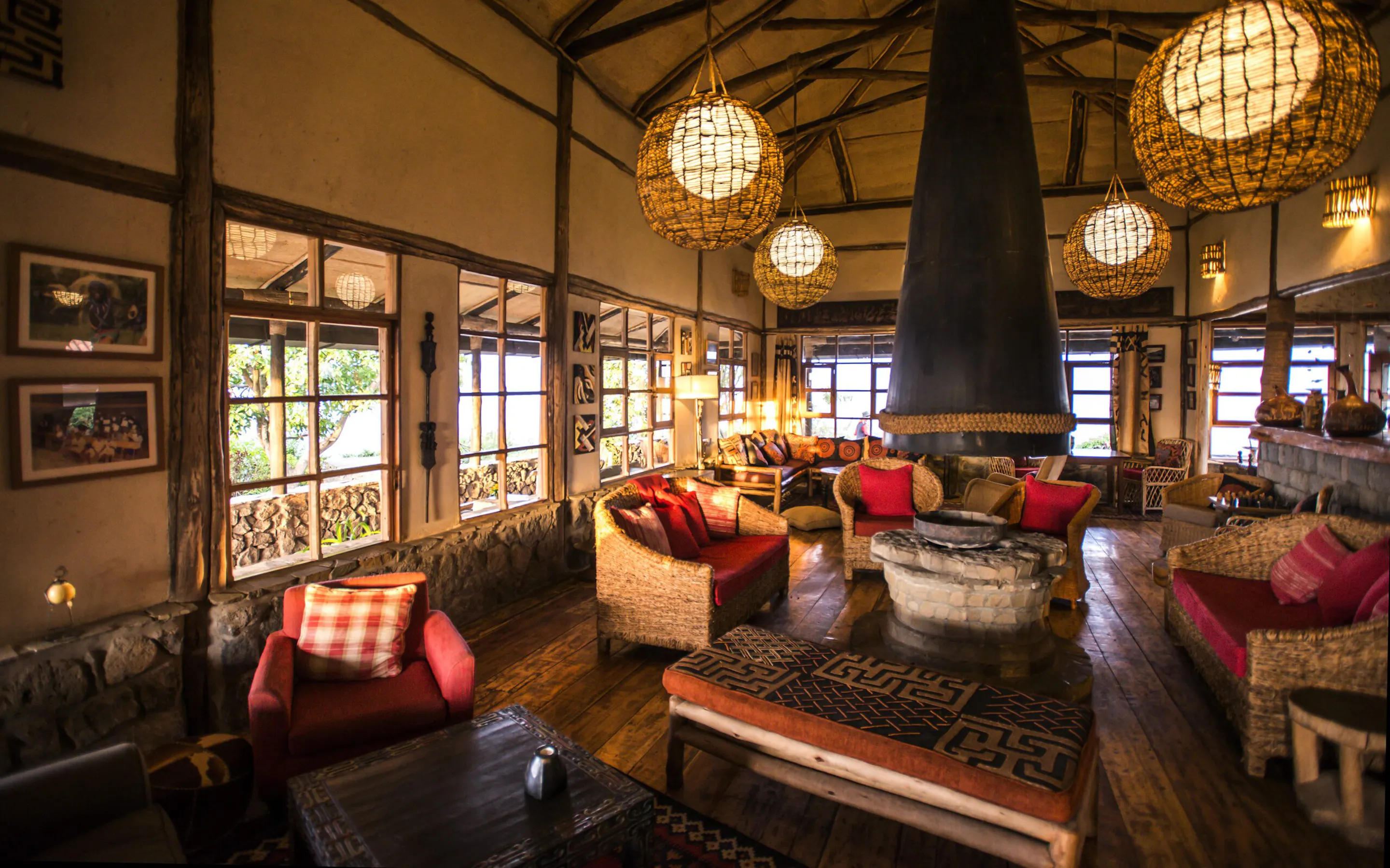 Warm lantern light fills the lounge at Virunga Lodge, with woven chairs, timber beams, and broad windows.