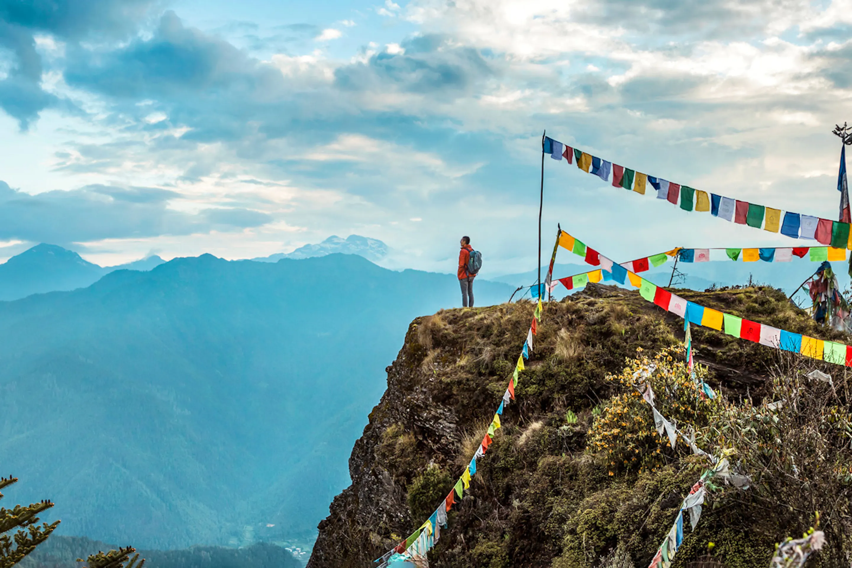 Prayer flags flutter from a rocky peak above COMO Uma Paro, with layers of blue mountains filling the distance.