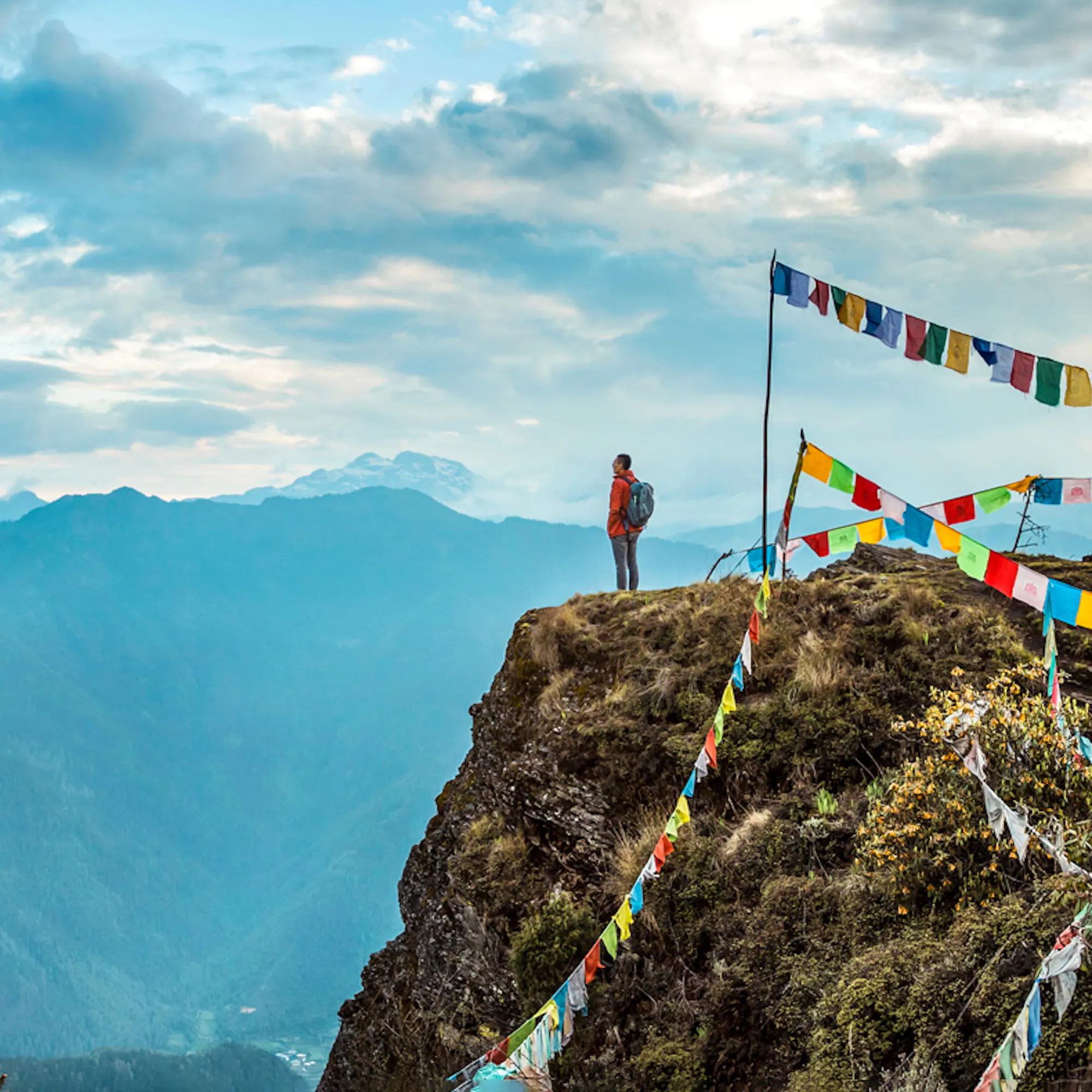 Prayer flags flutter from a rocky peak above COMO Uma Paro, with layers of blue mountains filling the distance.