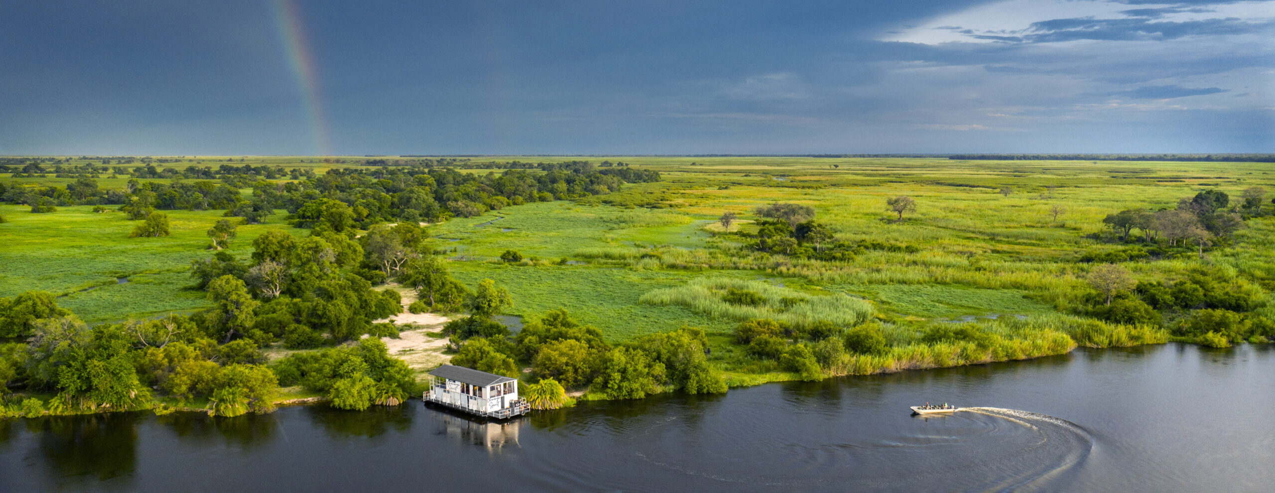 Aerial view of Okavango Spirit surrounded by winding channels, trees, and vivid green wetlands in Botswana.