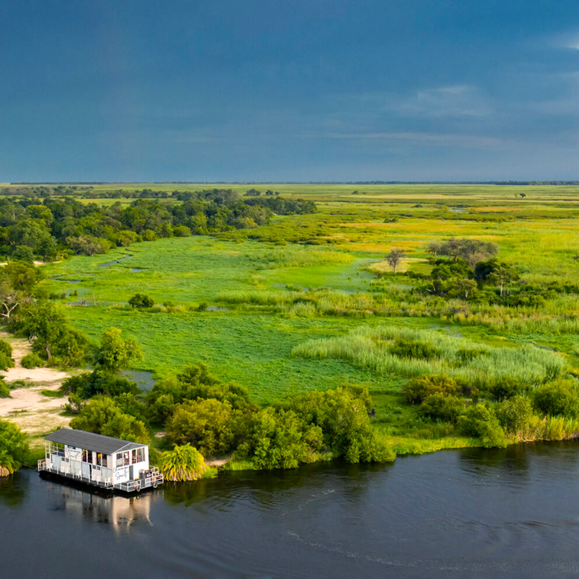 Aerial view of Okavango Spirit surrounded by winding channels, trees, and vivid green wetlands in Botswana.