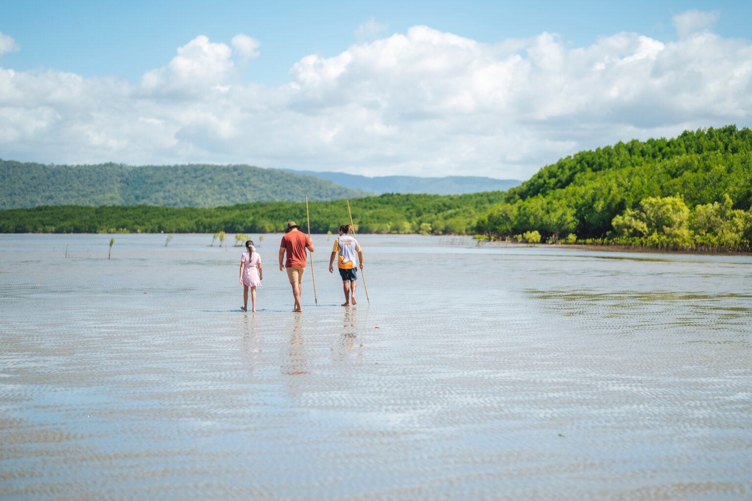 Two people walk through shallow water where the Daintree rainforest meets a quiet beach on Queensland's coast.
