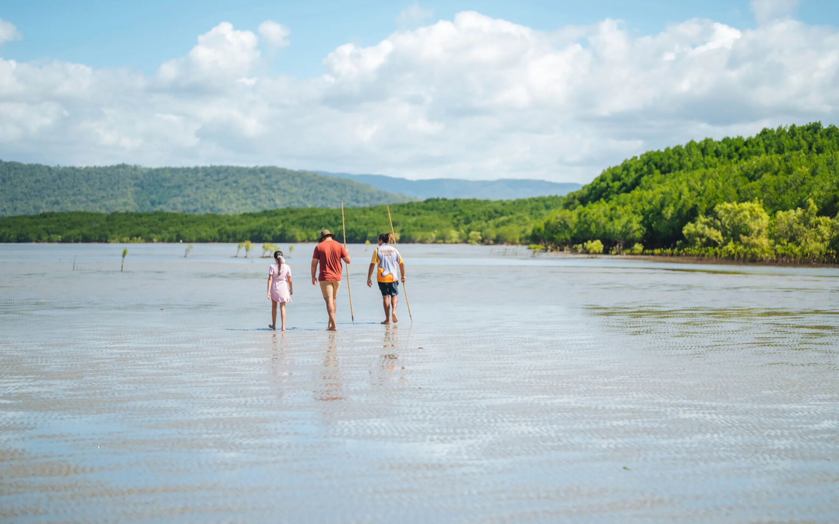 Two people walk through shallow water where the Daintree rainforest meets a quiet beach on Queensland's coast.