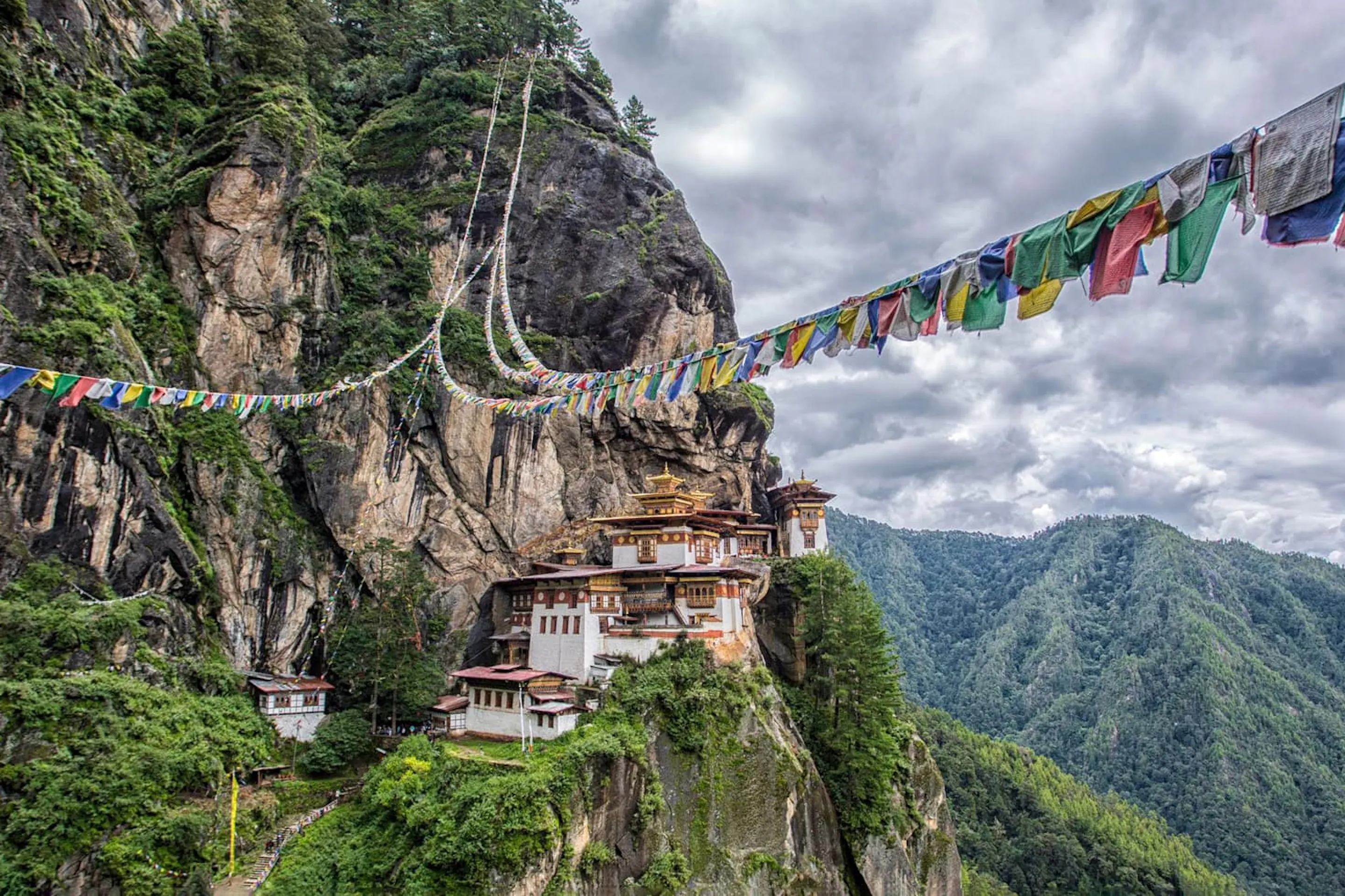 Tiger's Nest Monastery clings to a sheer cliff in Paro, with prayer flags and cloud-filled valleys beyond.