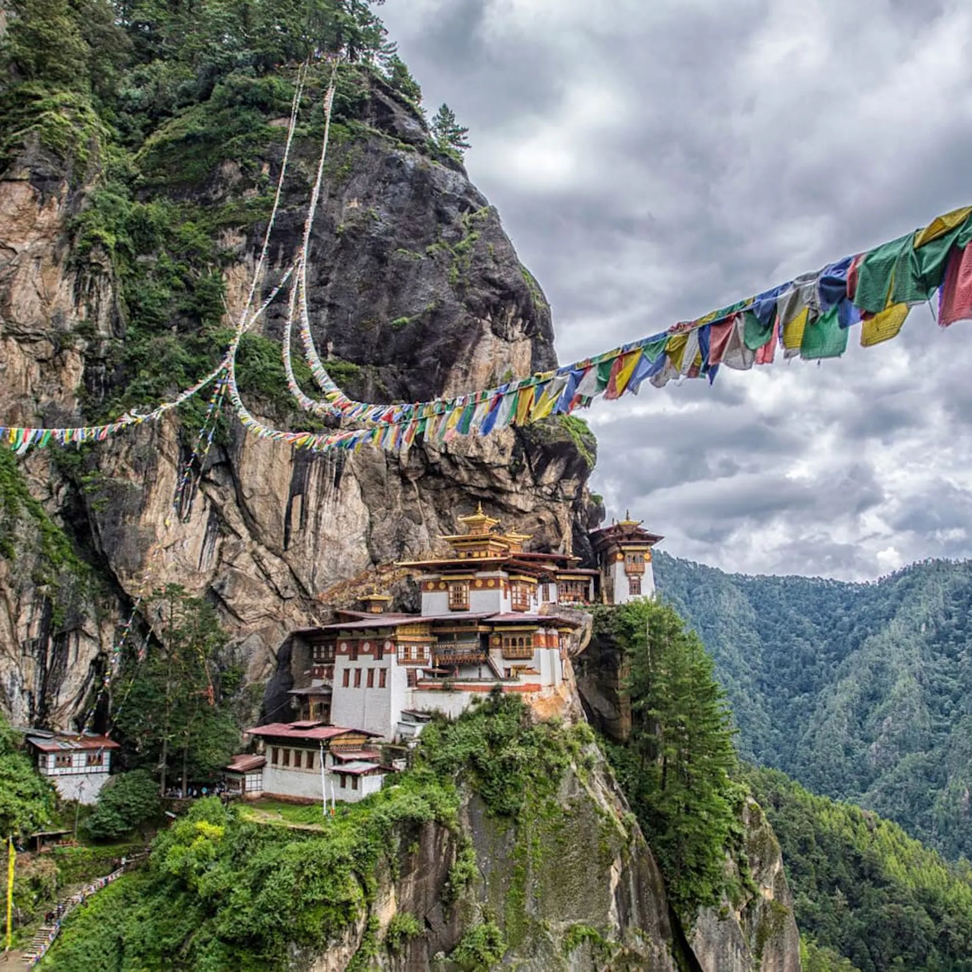 Tiger's Nest Monastery clings to a sheer cliff in Paro, with prayer flags and cloud-filled valleys beyond.