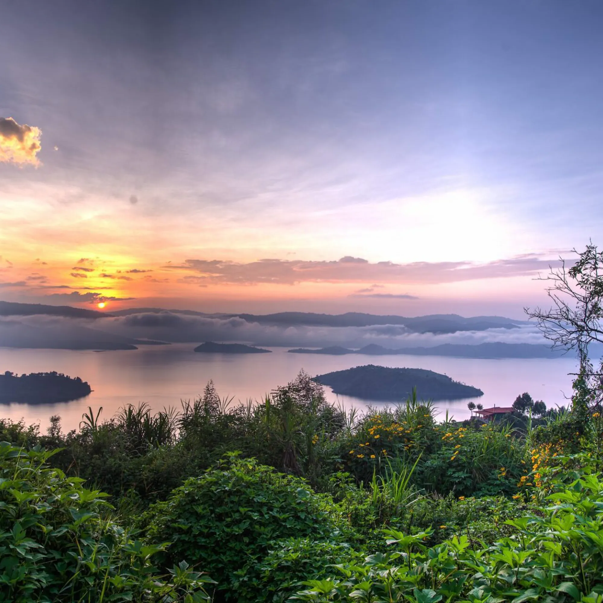 Soft pink light settles over the lakes below Virunga Lodge, framed by leafy trees and distant Rwanda hills.