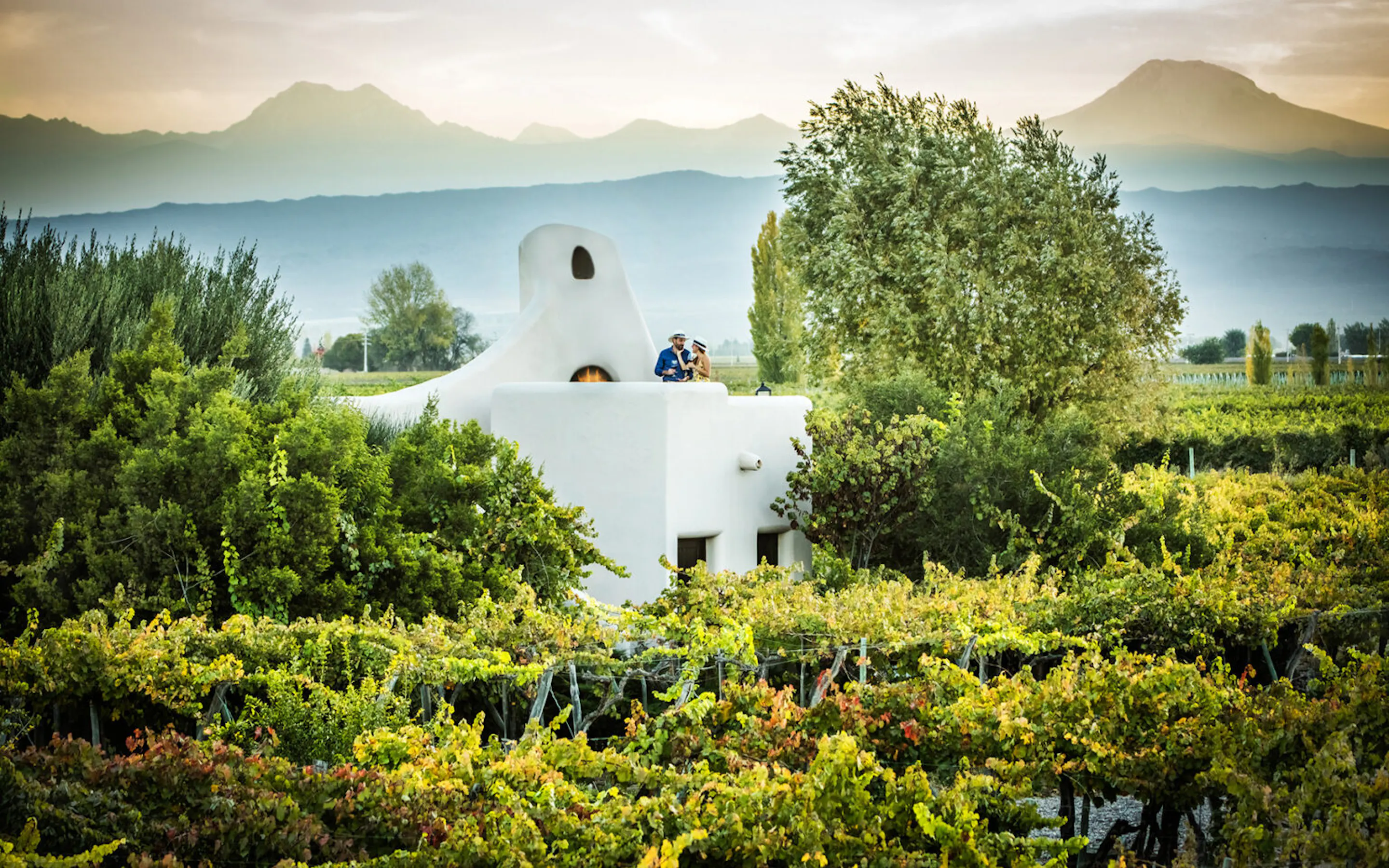 A white villa sits among vineyard rows at Cavas Wine Lodge in Mendoza, with dry hills rising in the distance.