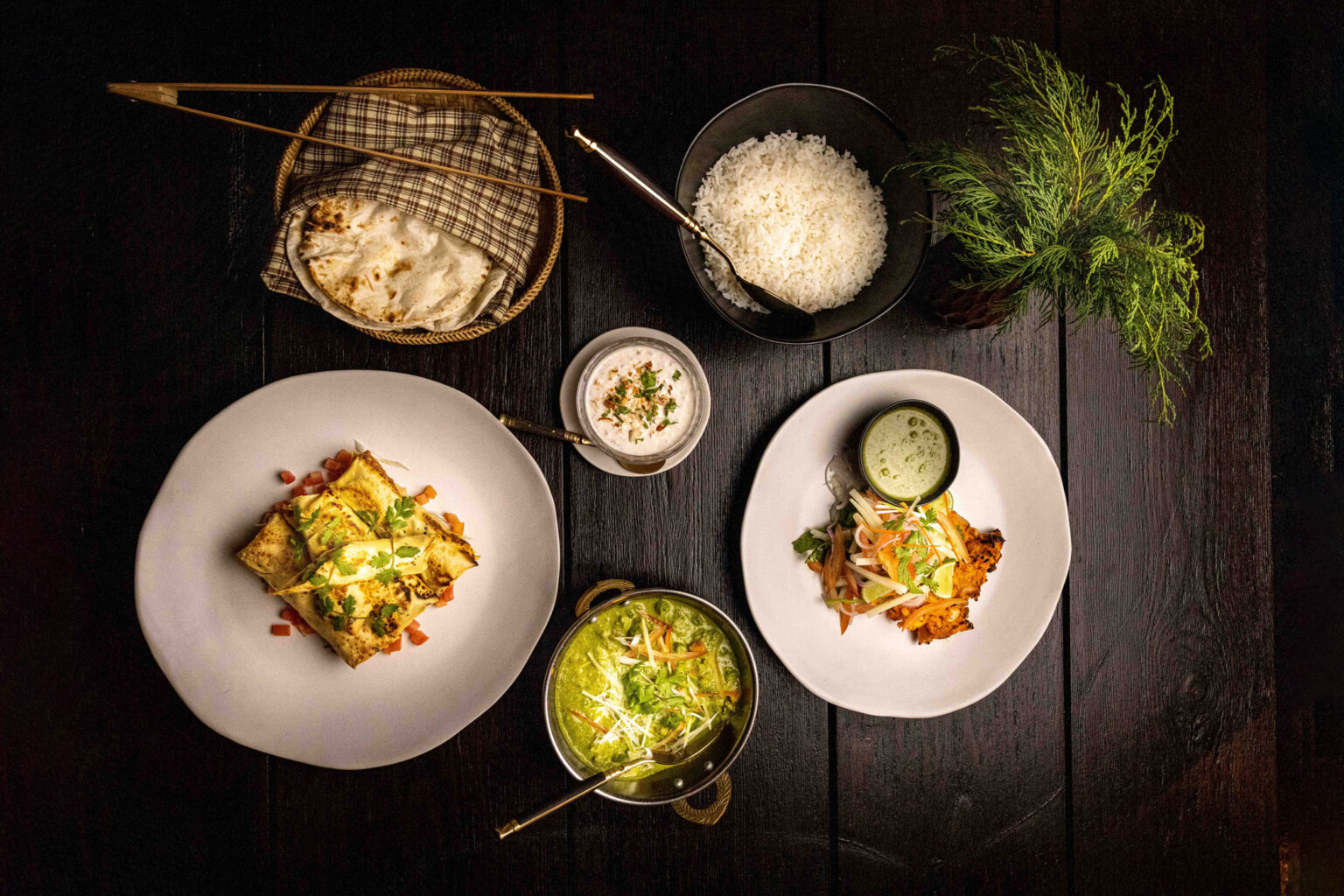 Plates of colorful food and woven baskets are arranged on a dark table at Gangtey Lodge, ready for a shared meal.