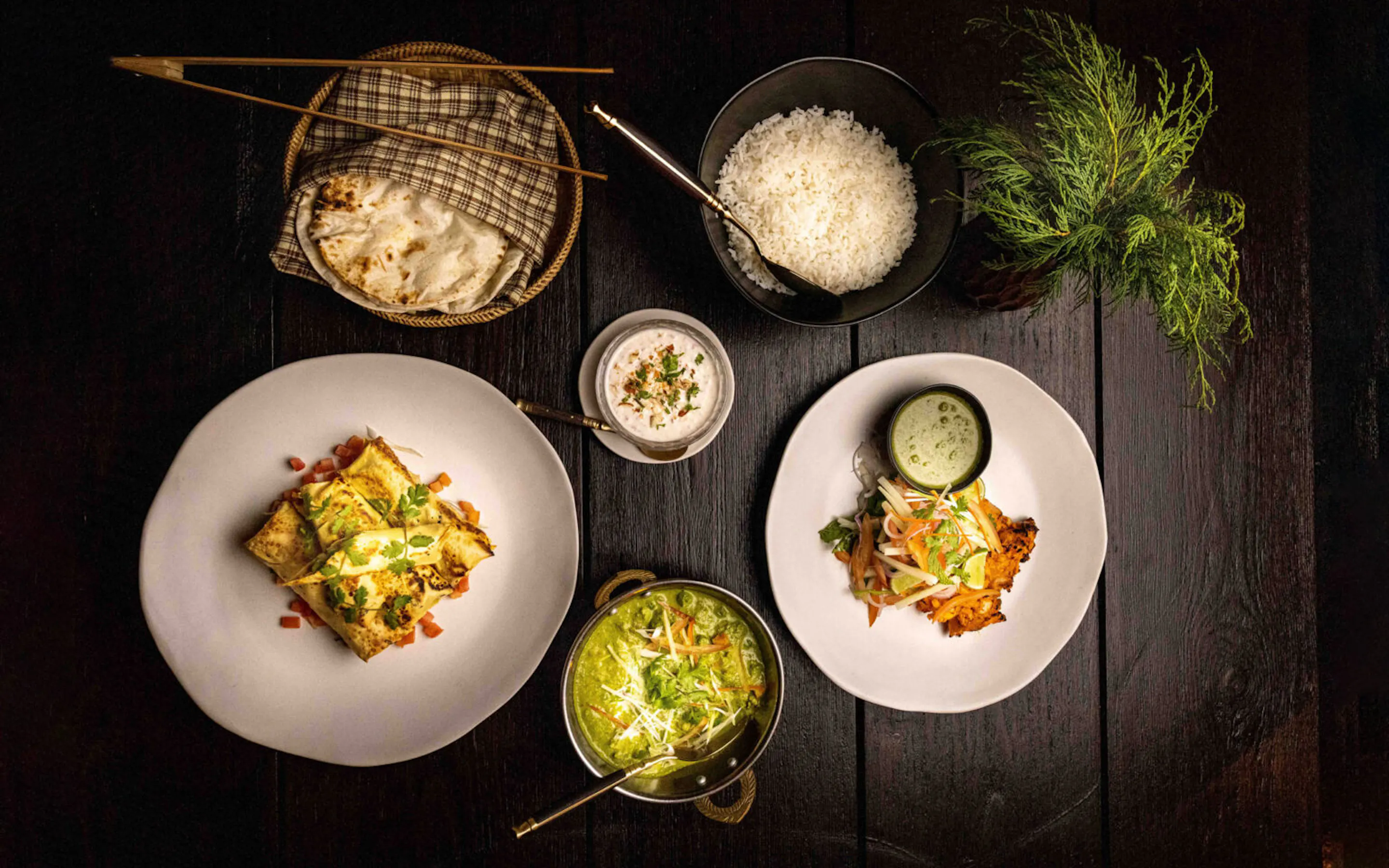 Plates of colorful food and woven baskets are arranged on a dark table at Gangtey Lodge, ready for a shared meal.