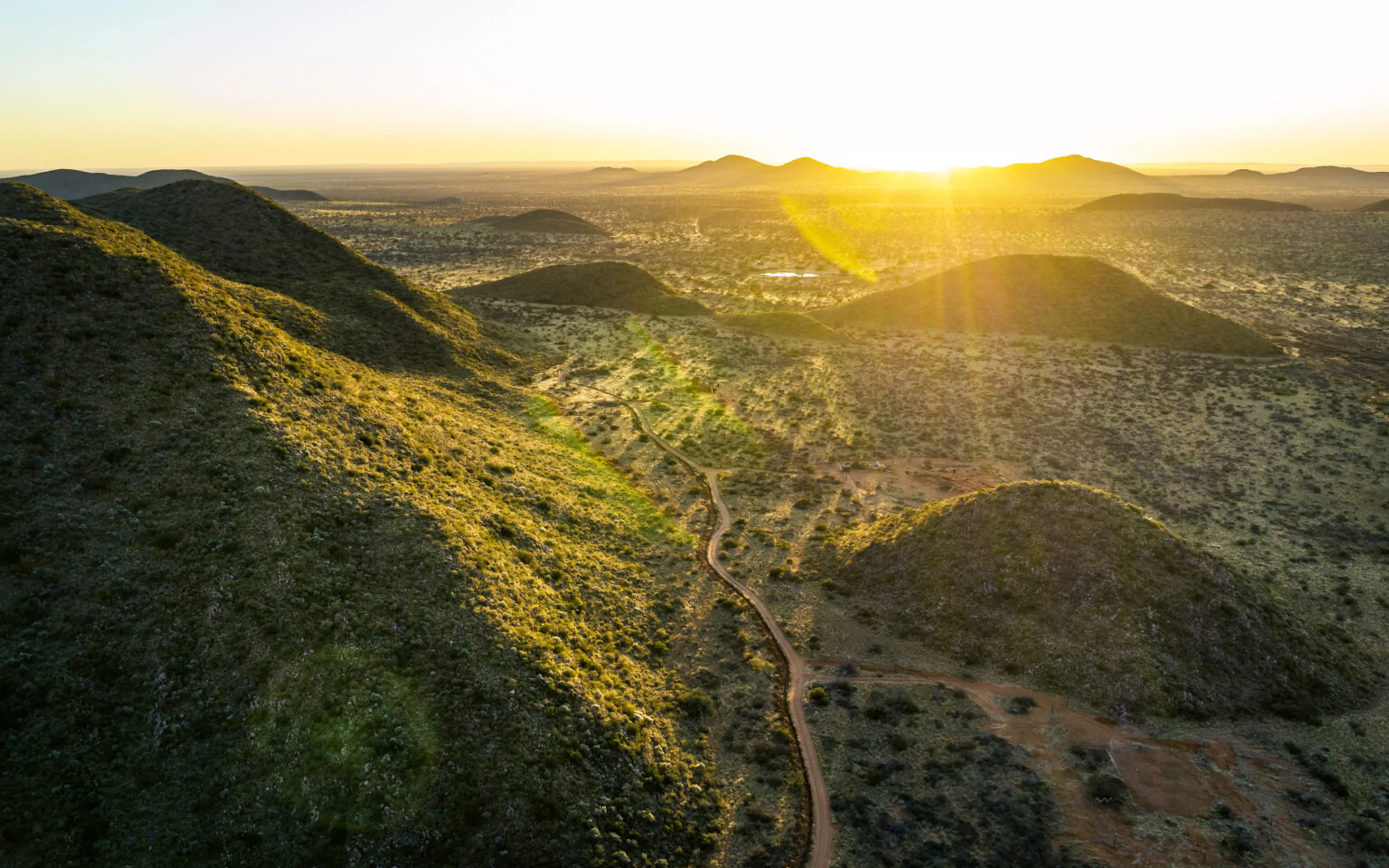 A tented camp sits beneath mountains at Loapi in South Africa's Southern Kalahari, with open ground in front.