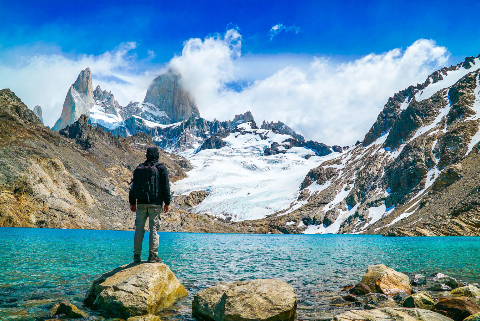 A lone traveler standing before Fitz Roy and a turquoise lake against the backdrop of El Chalten, Patagonia.