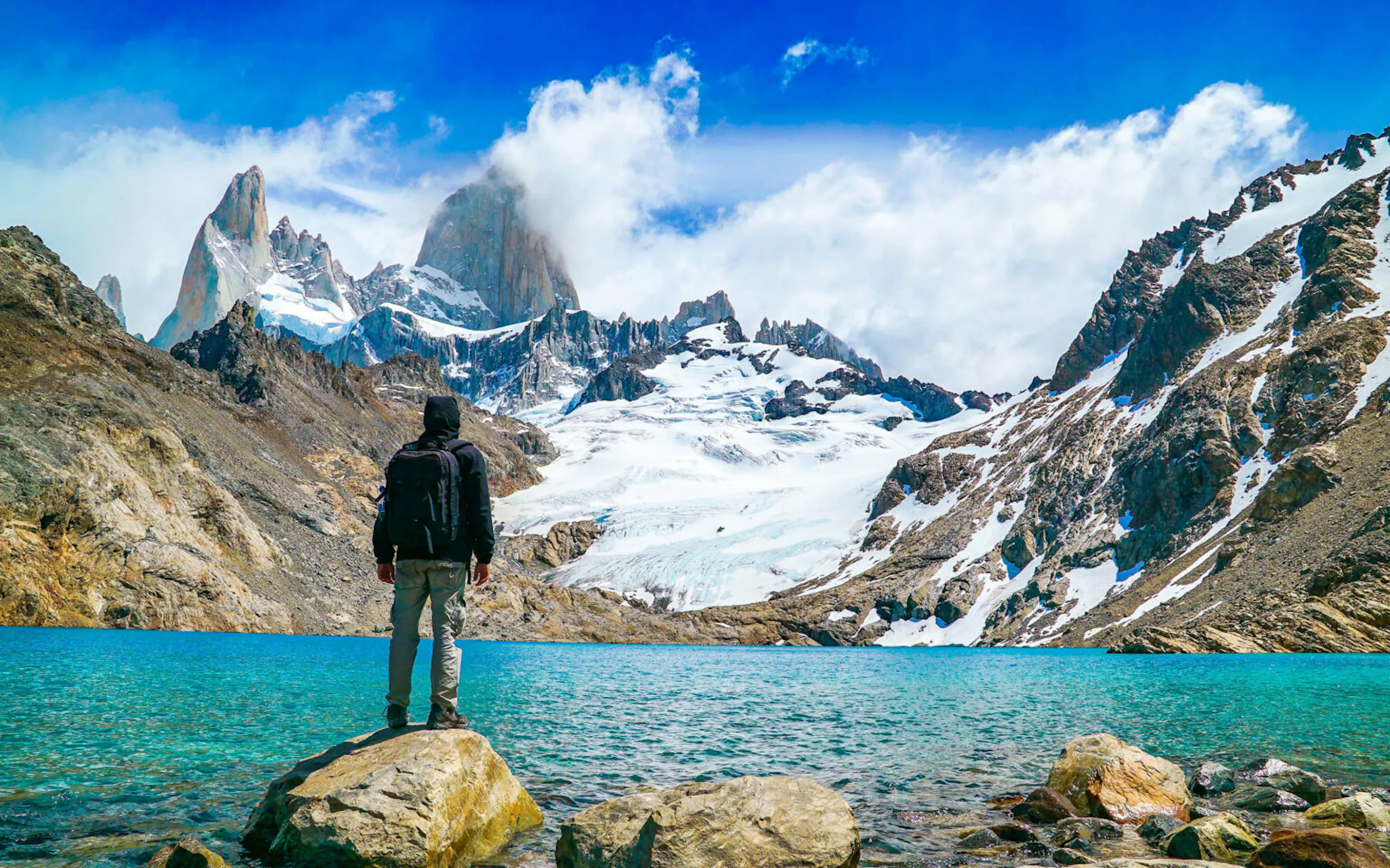 A lone traveler standing before Fitz Roy and a turquoise lake against the backdrop of El Chalten, Patagonia.