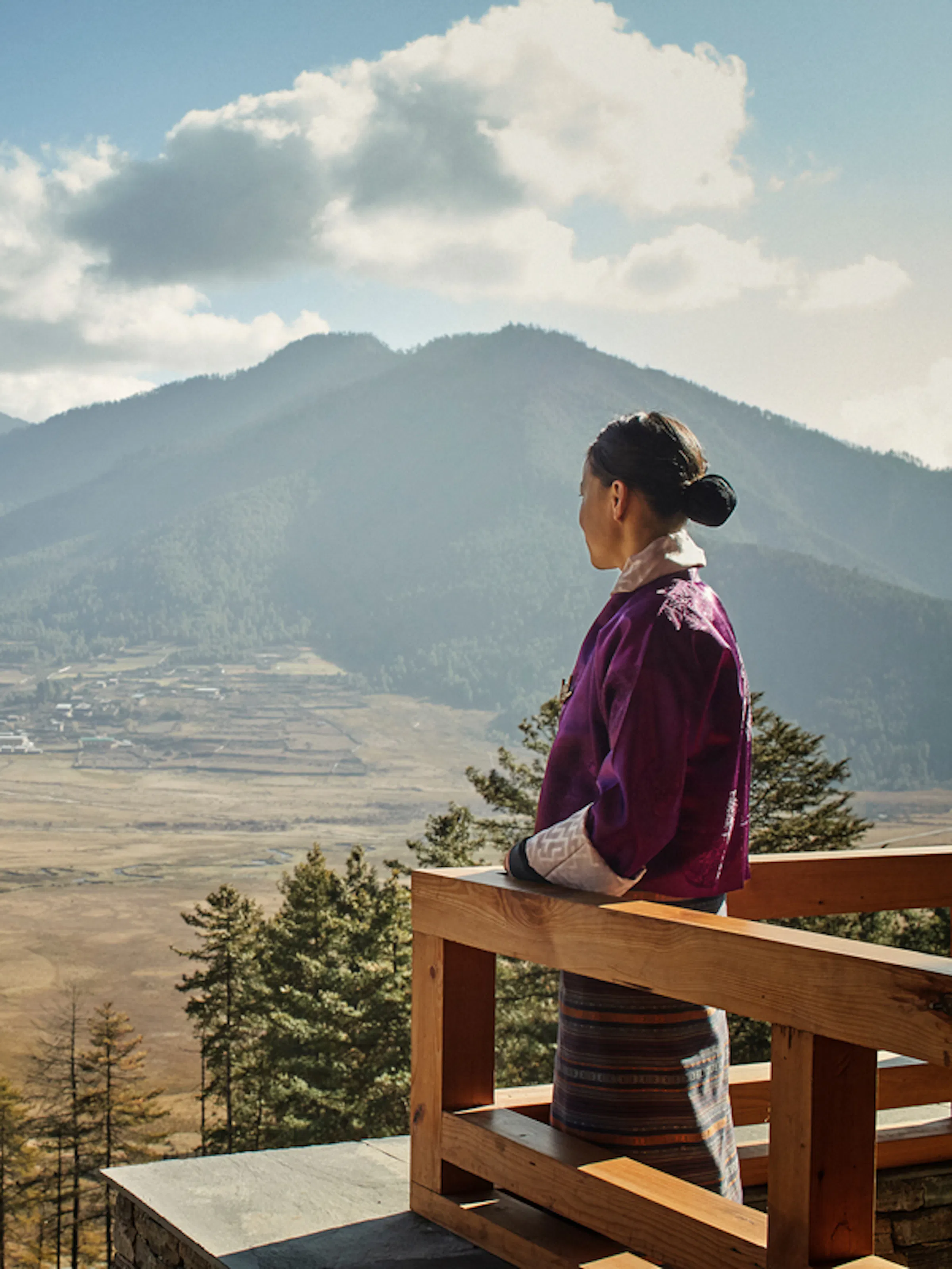 A host looks out over the wide Phobjikha Valley from Six Senses Gangtey, framed by terrace and mountains.