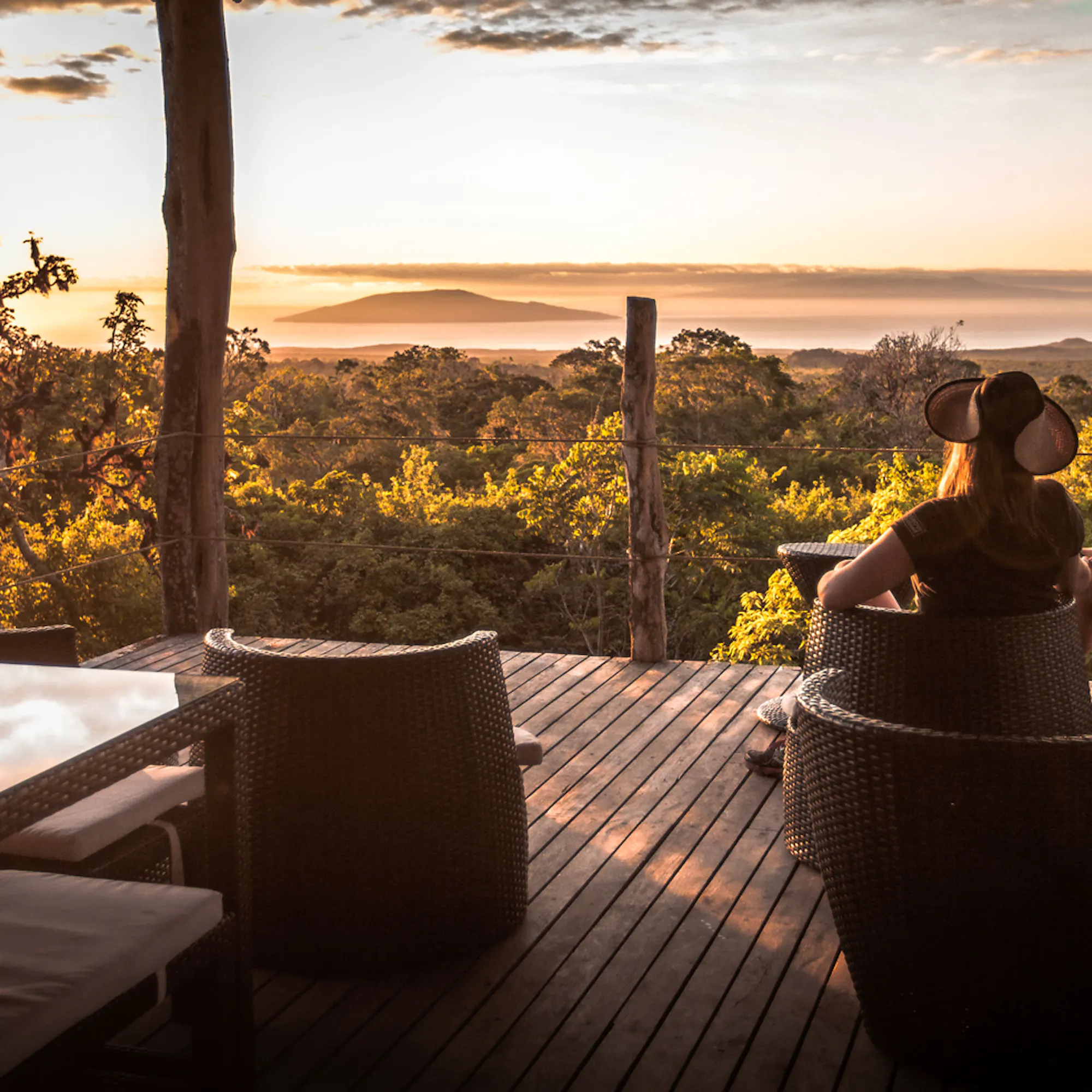 A couple relaxes on a deck overlooking the Galapagos, with distant islands and low water below the viewpoint.
