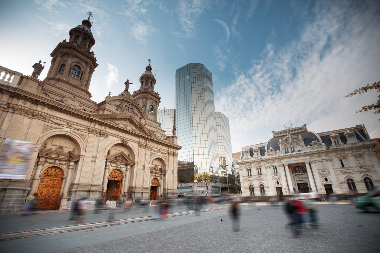Historic buildings and glass towers rise in central Santiago, with a partly cloudy sky and layered city streets below.
