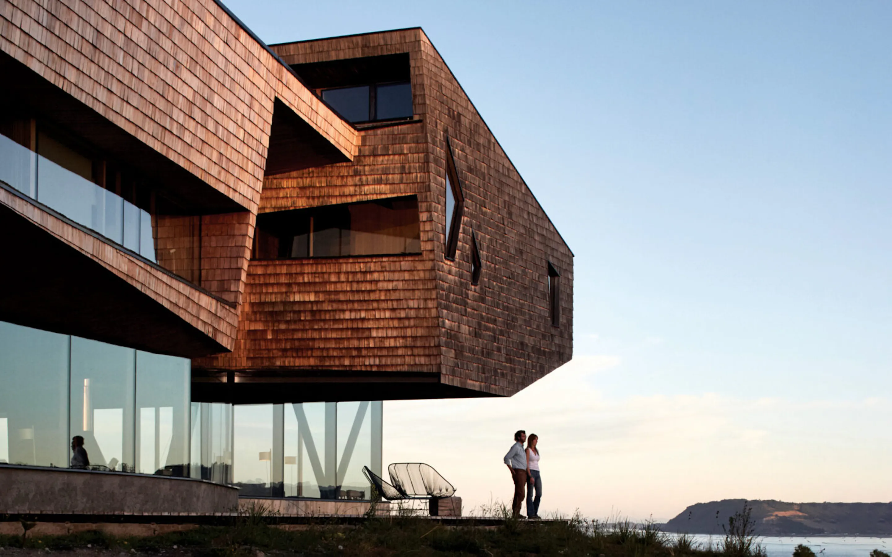 A timber lodge living room at Tierra Chiloe opens toward water views, with dark beams and wide windows inside.