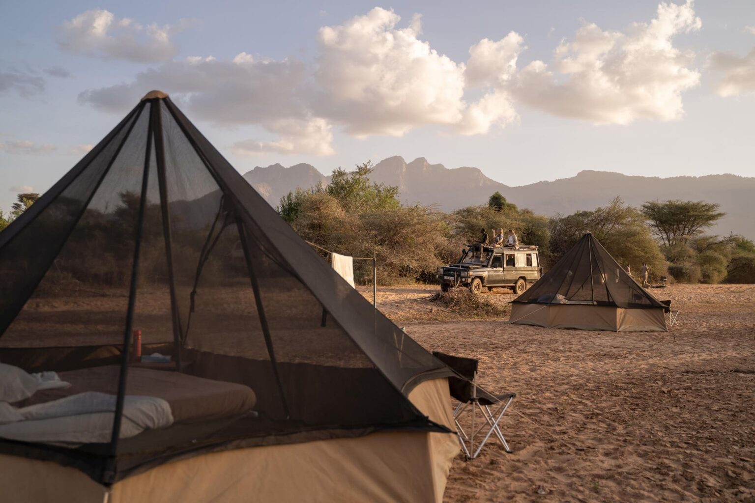 Guests drive past their fly camp in northern Kenya, where canvas tents sit beside wide grasslands at dusk.