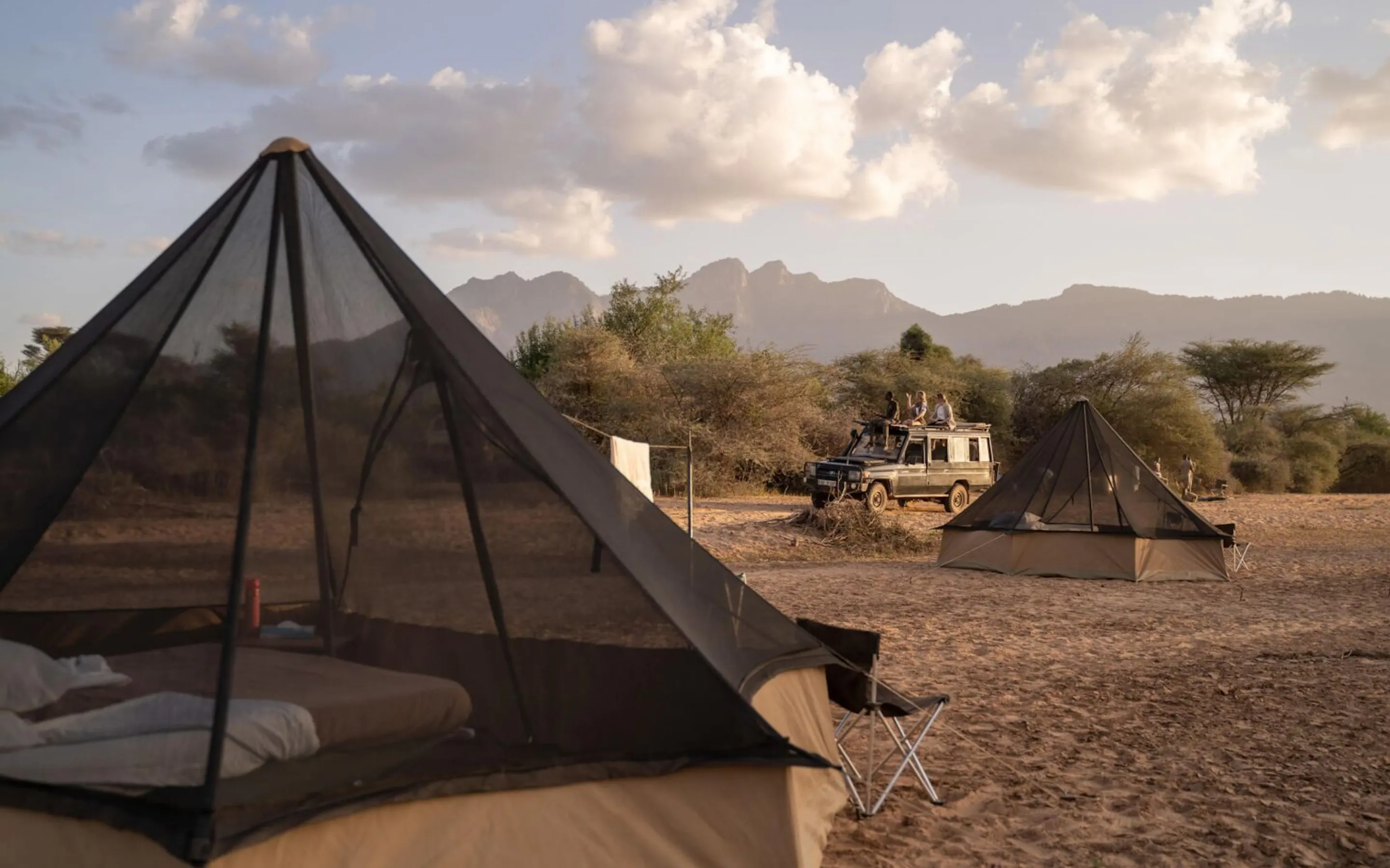 Guests drive past their fly camp in northern Kenya, where canvas tents sit beside wide grasslands at dusk.