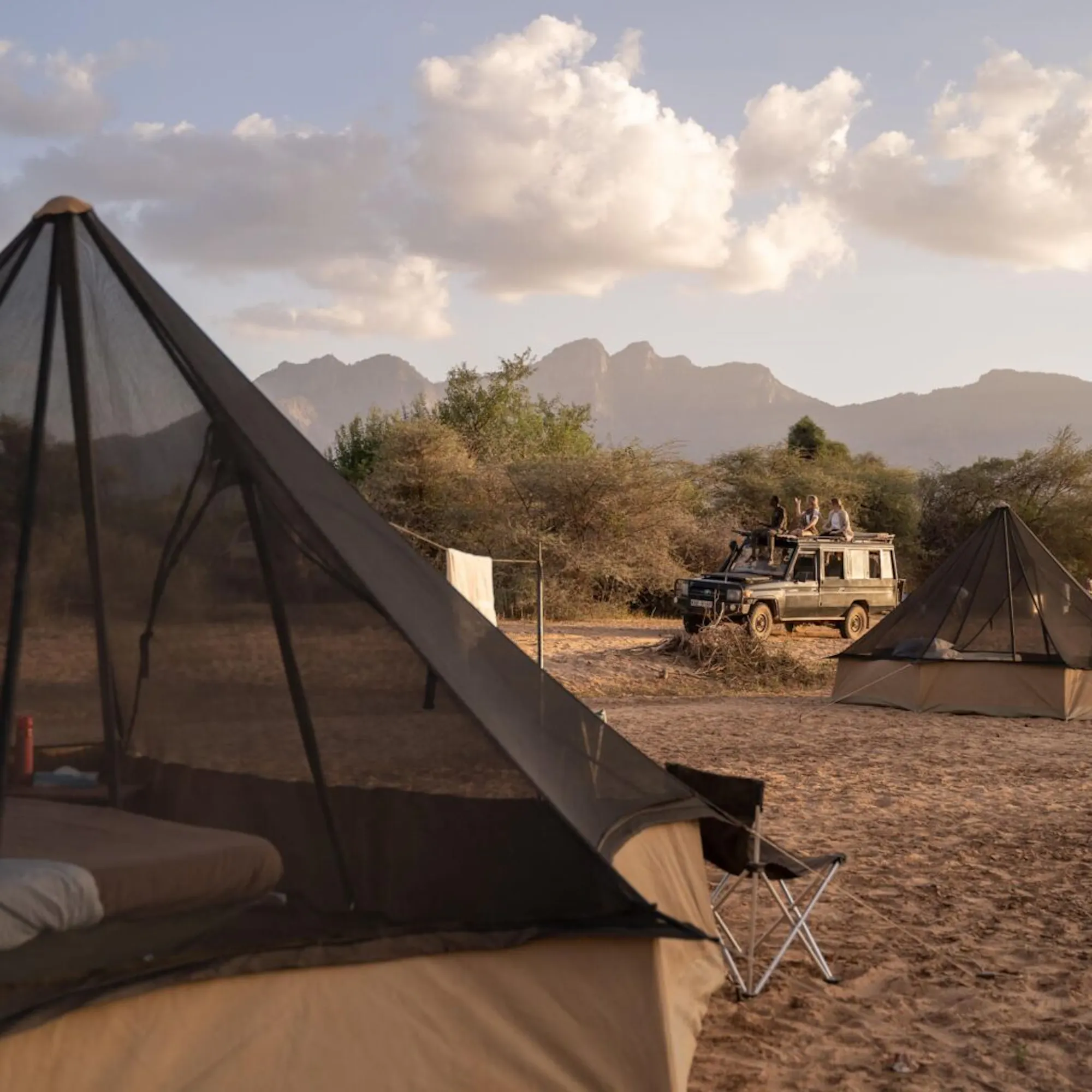 Guests drive past their fly camp in northern Kenya, where canvas tents sit beside wide grasslands at dusk.