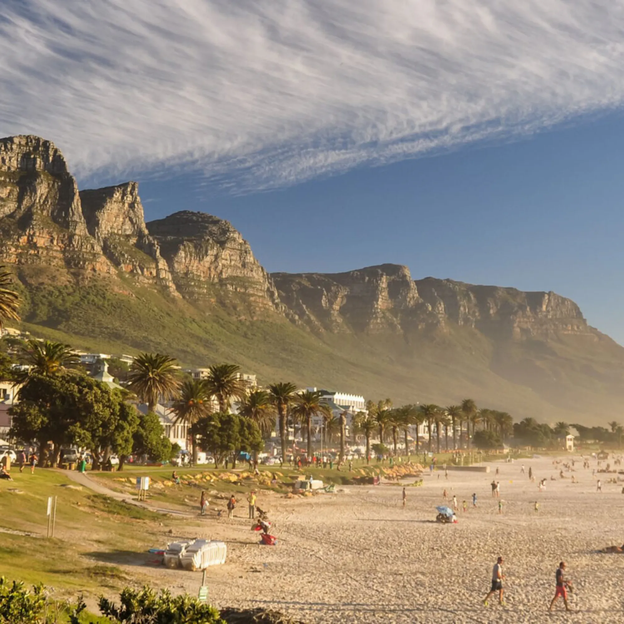 Camps Bay beach stretches beneath the Twelve Apostles near Cape Town, with pale sand and waves in the foreground.
