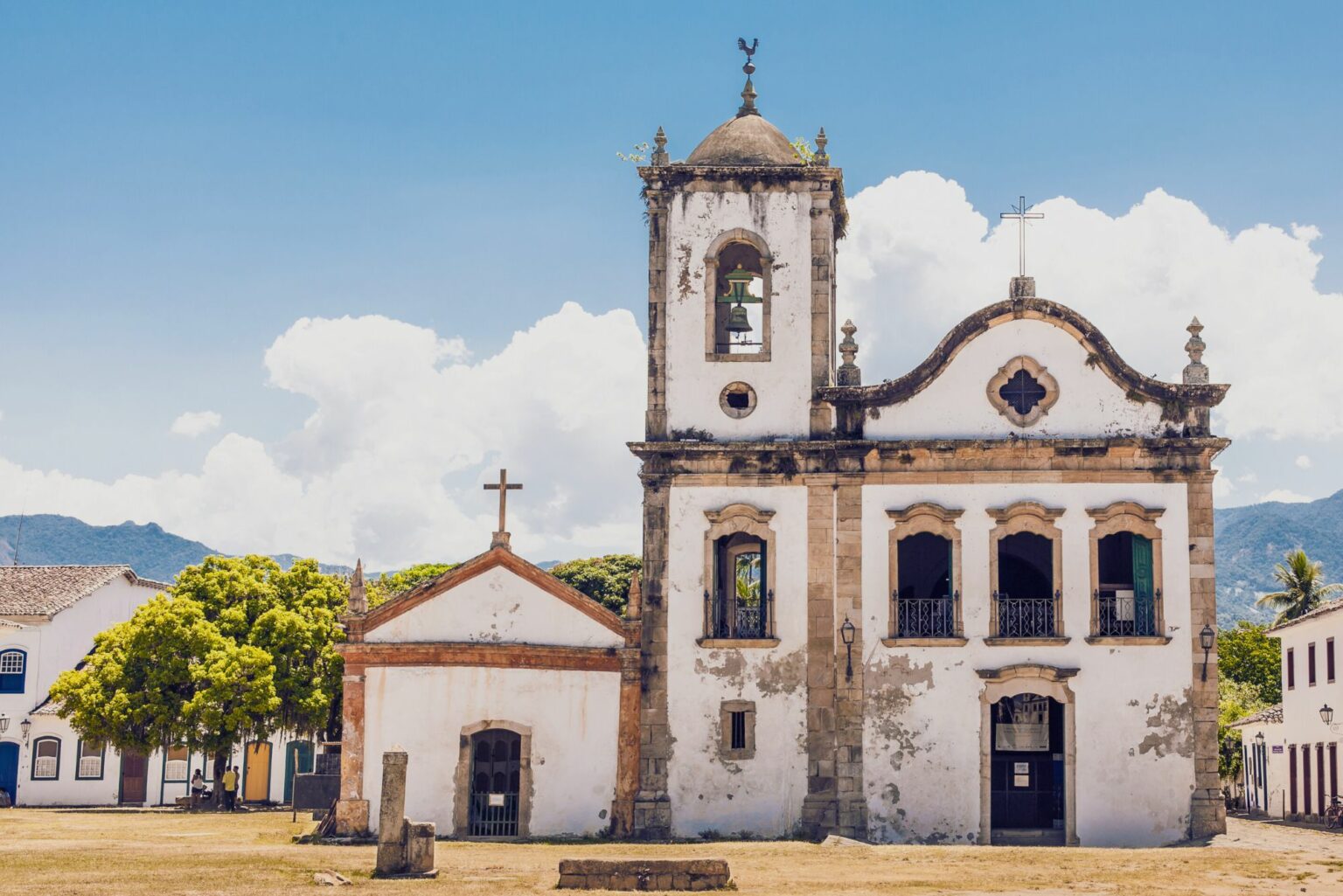Paraty's whitewashed church stands against a blue sky, with quiet streets and colonial facades around the square.