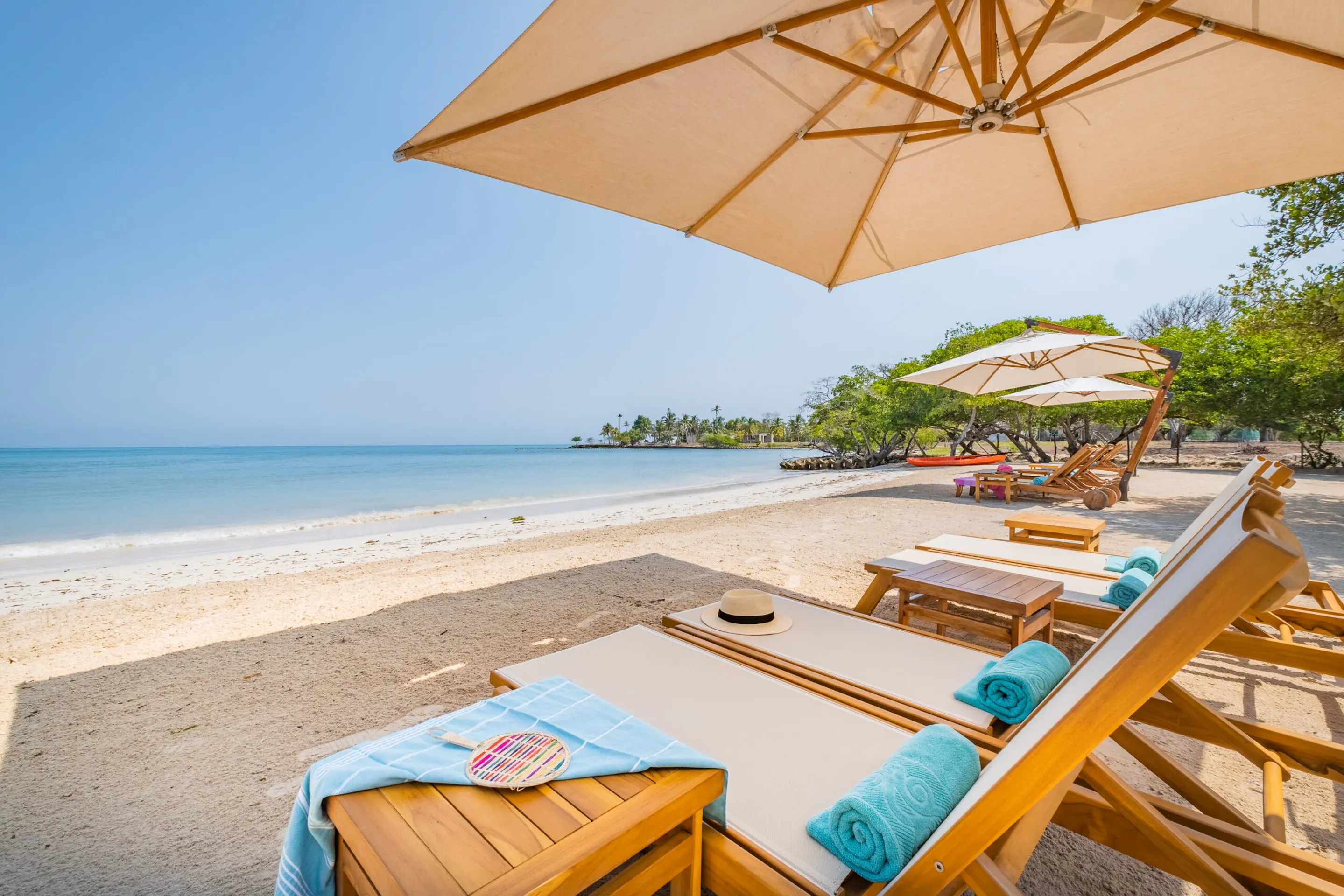 Private umbrellas and loungers line Casa San Agustin's beach, facing calm turquoise water, pale sand, and low tide.