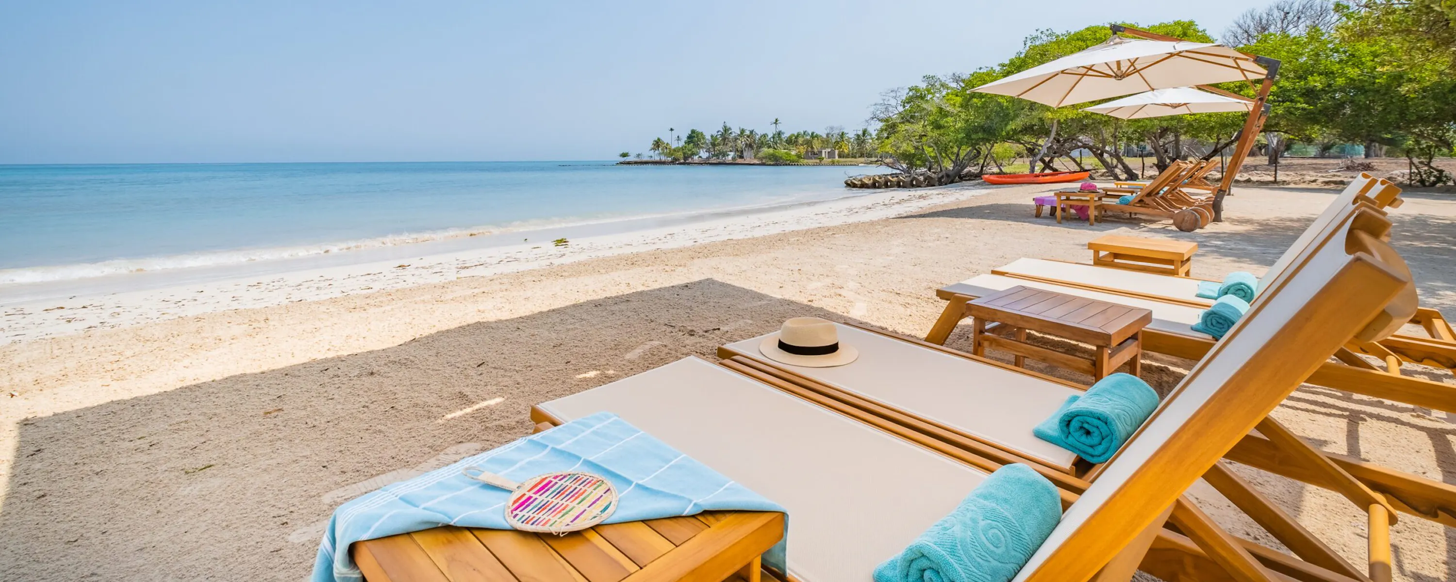 Private umbrellas and loungers line Casa San Agustin's beach, facing calm turquoise water, pale sand, and low tide.