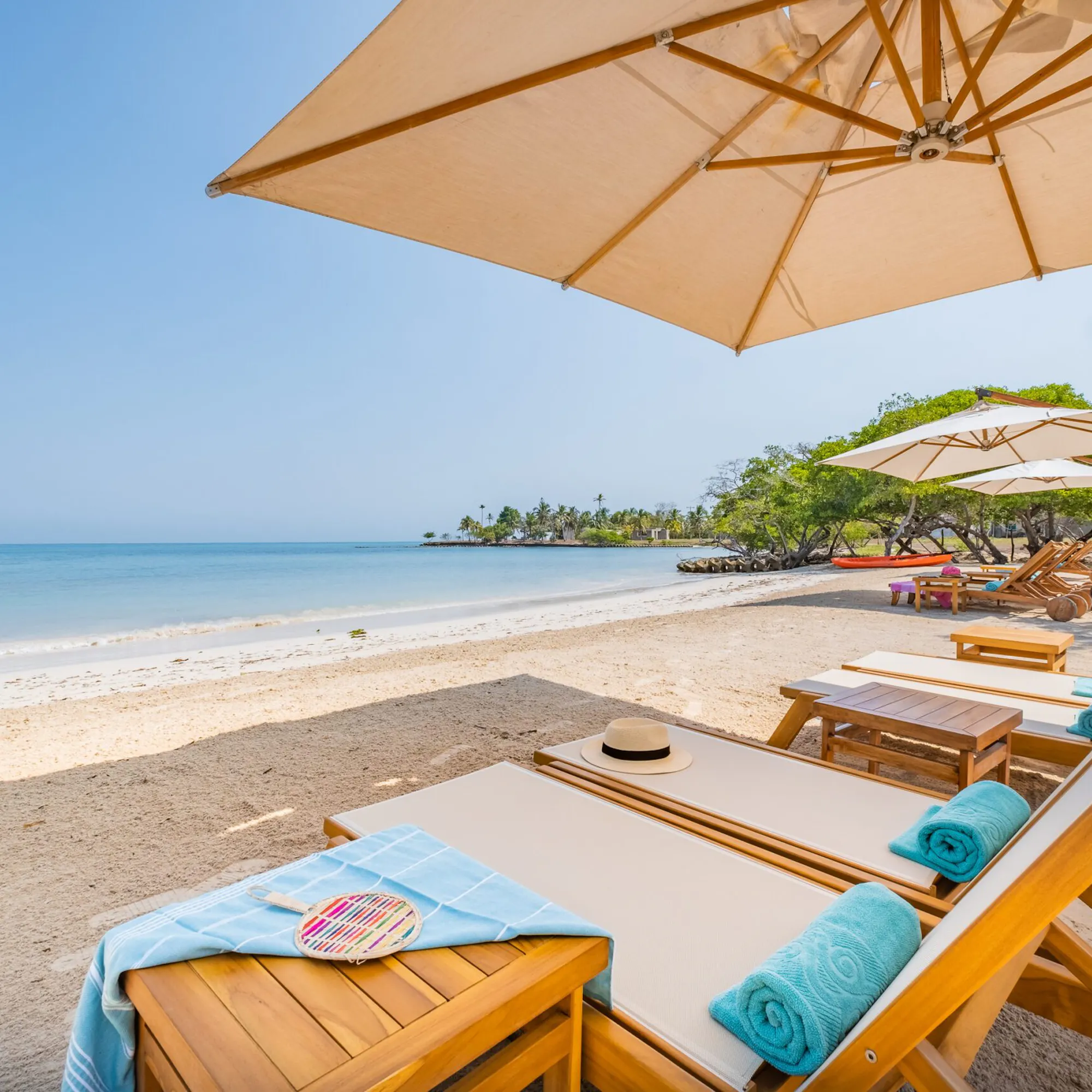 Private umbrellas and loungers line Casa San Agustin's beach, facing calm turquoise water, pale sand, and low tide.