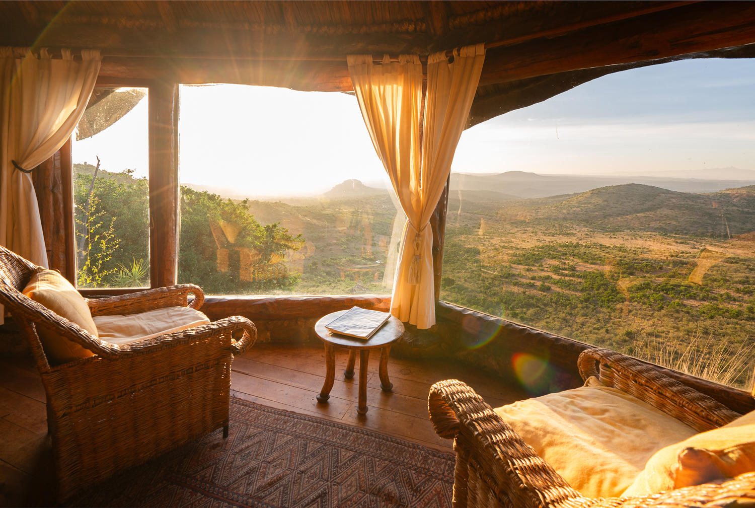 Morning light fills a lodge sitting area overlooking Laikipia’s hills, with two armchairs and a small table by the window.