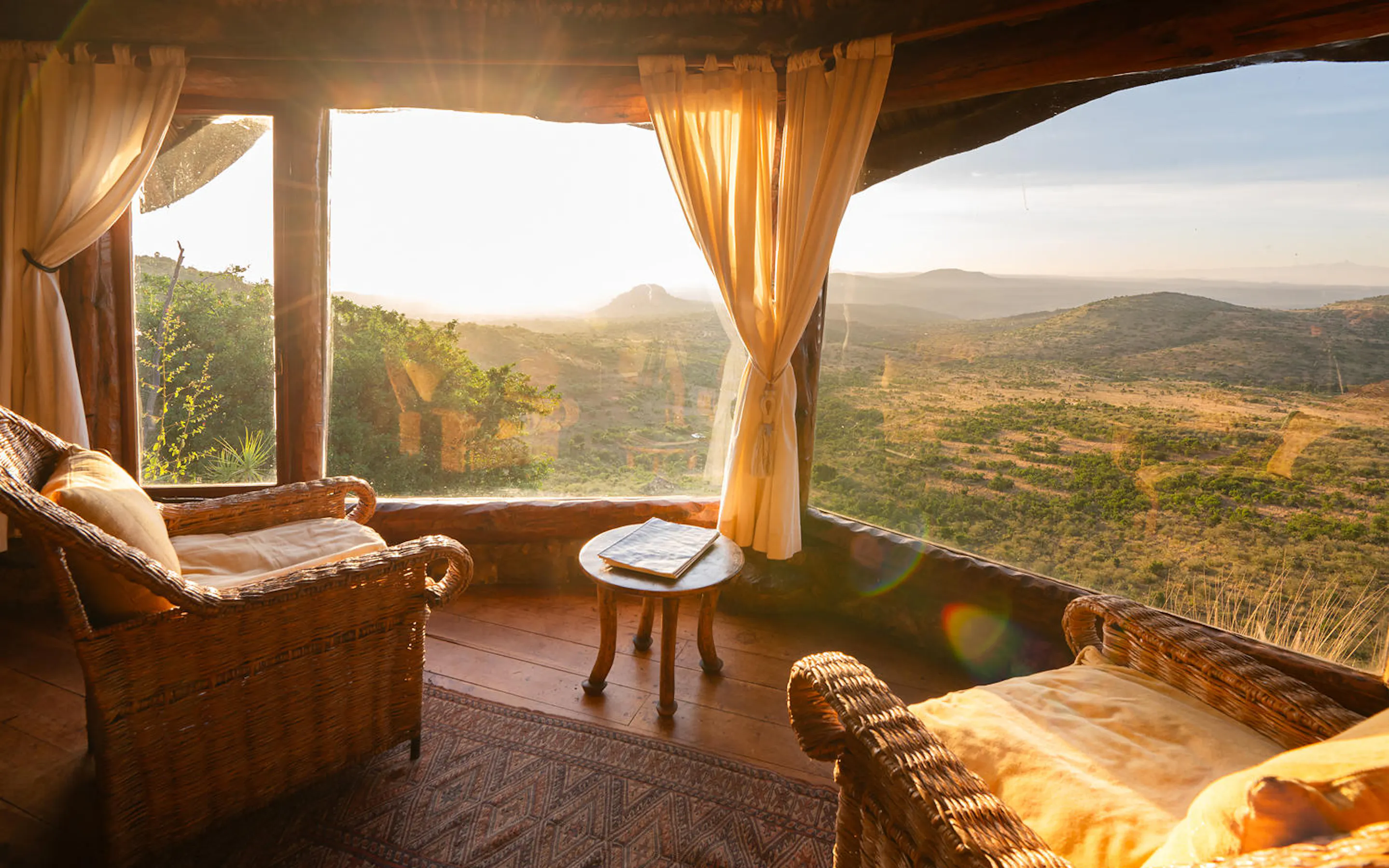 Morning light fills a lodge sitting area overlooking Laikipia’s hills, with two armchairs and a small table by the window.
