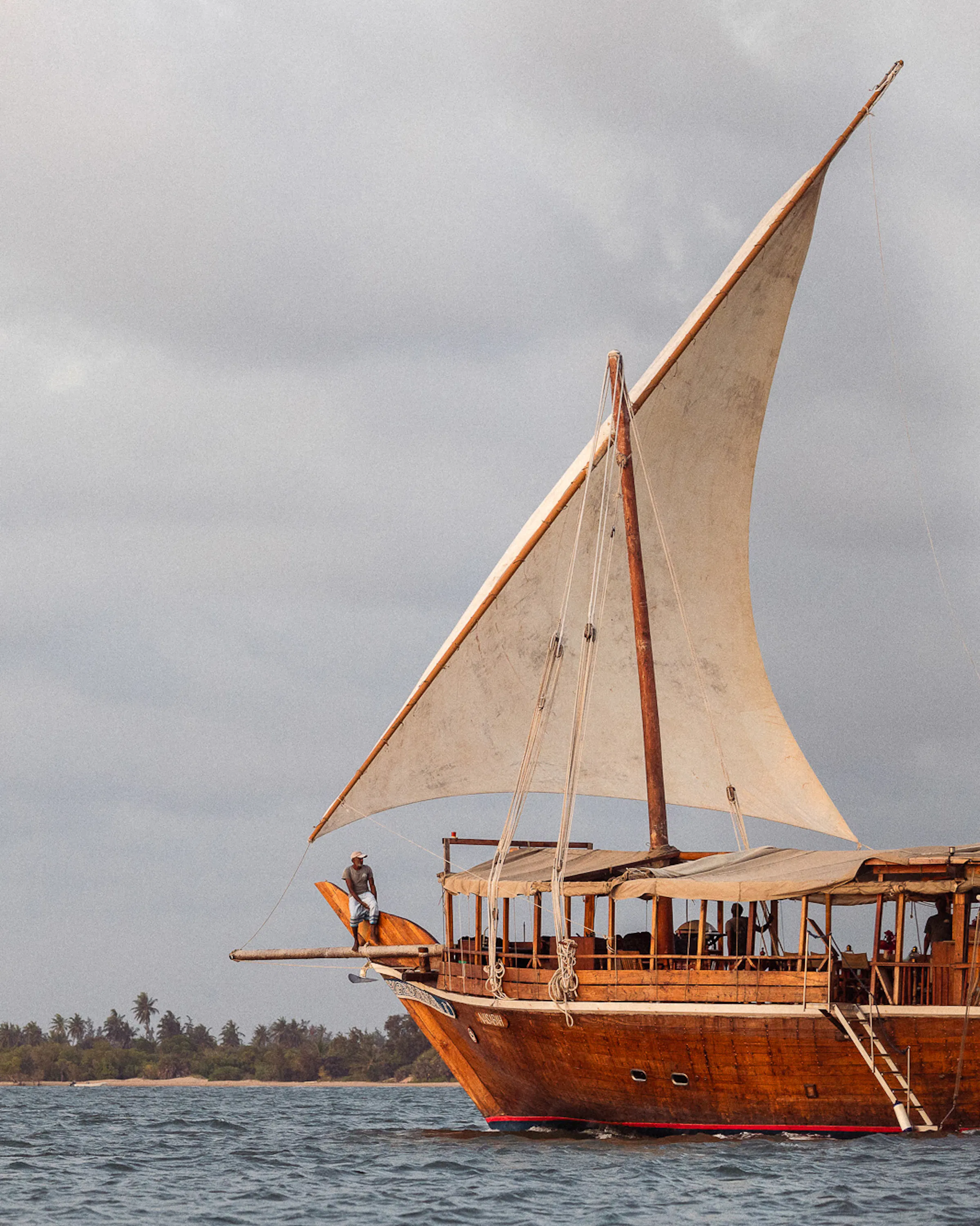 A traditional dhow sails off Lamu beneath moody clouds, its wooden hull and tall mast rising above the sea.