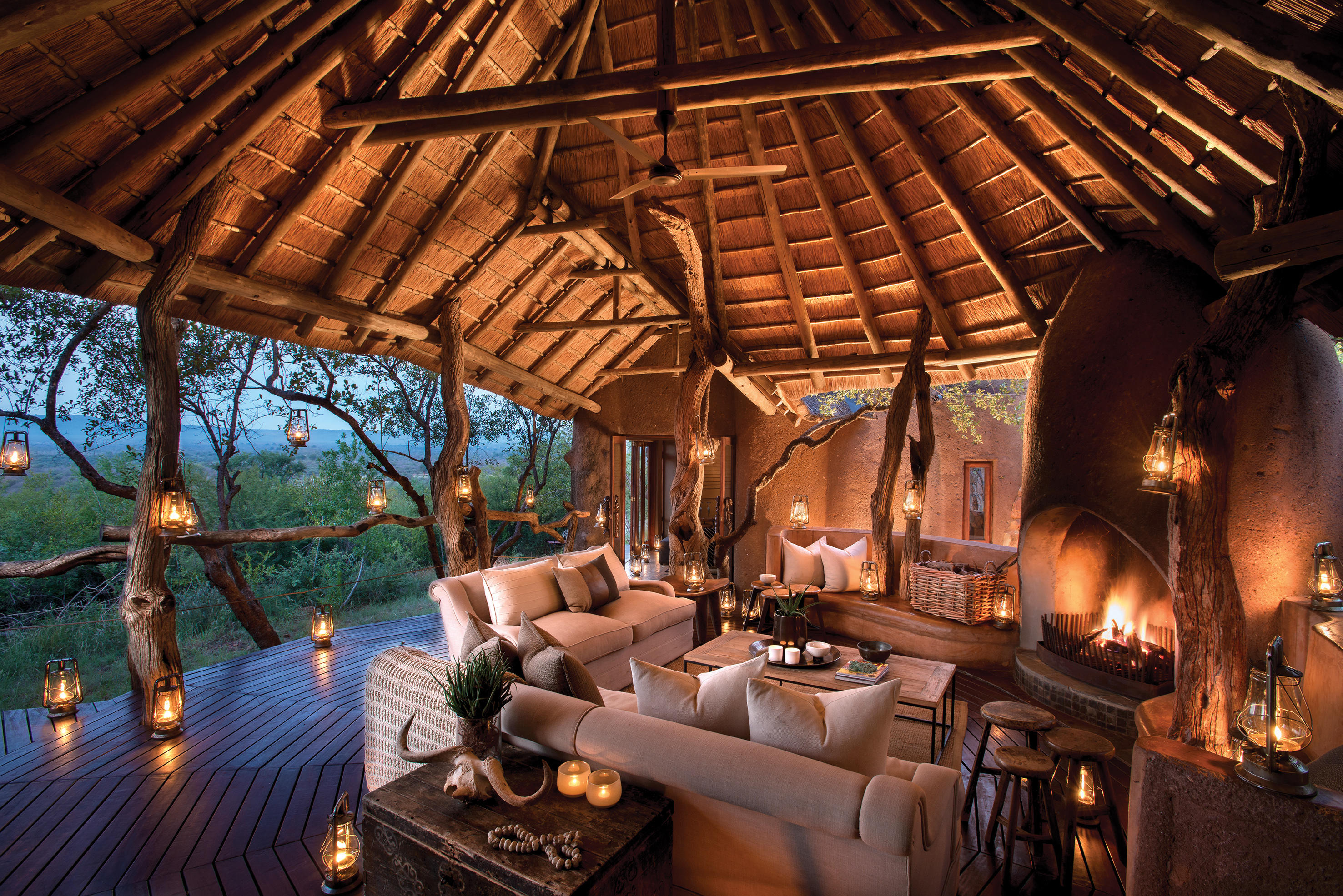 Lanterns glow around a cozy lounge and fireplace beneath a high thatched roof at Dithaba Camp in Madikwe.