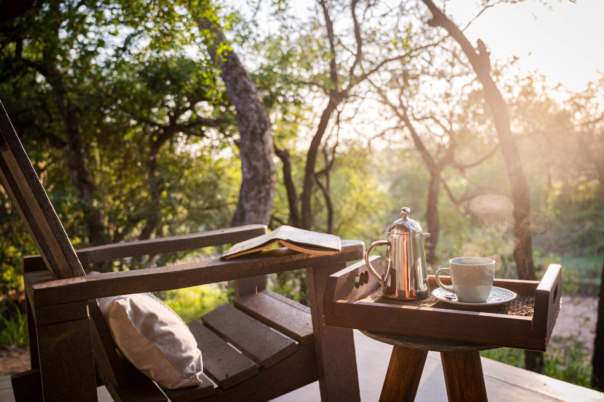 A breakfast tray sits on a timber deck at Kambaku, with warm light filtering through the surrounding trees.