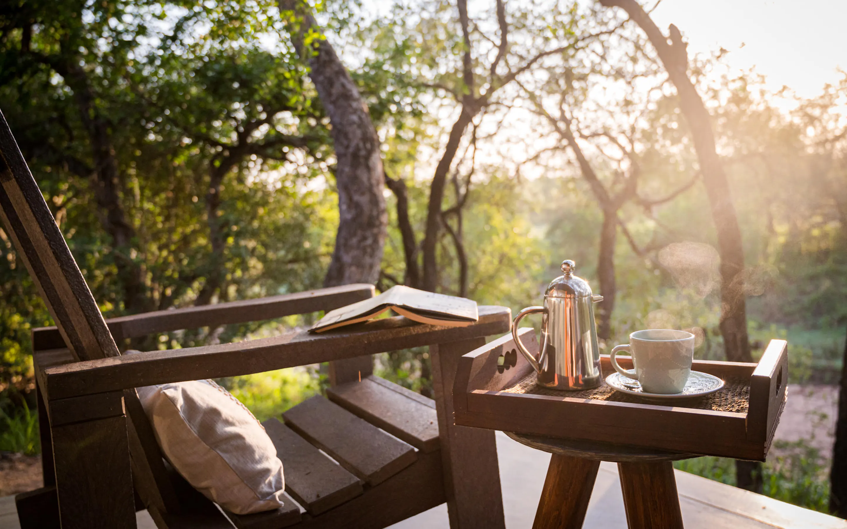 A breakfast tray sits on a timber deck at Kambaku, with warm light filtering through the surrounding trees.