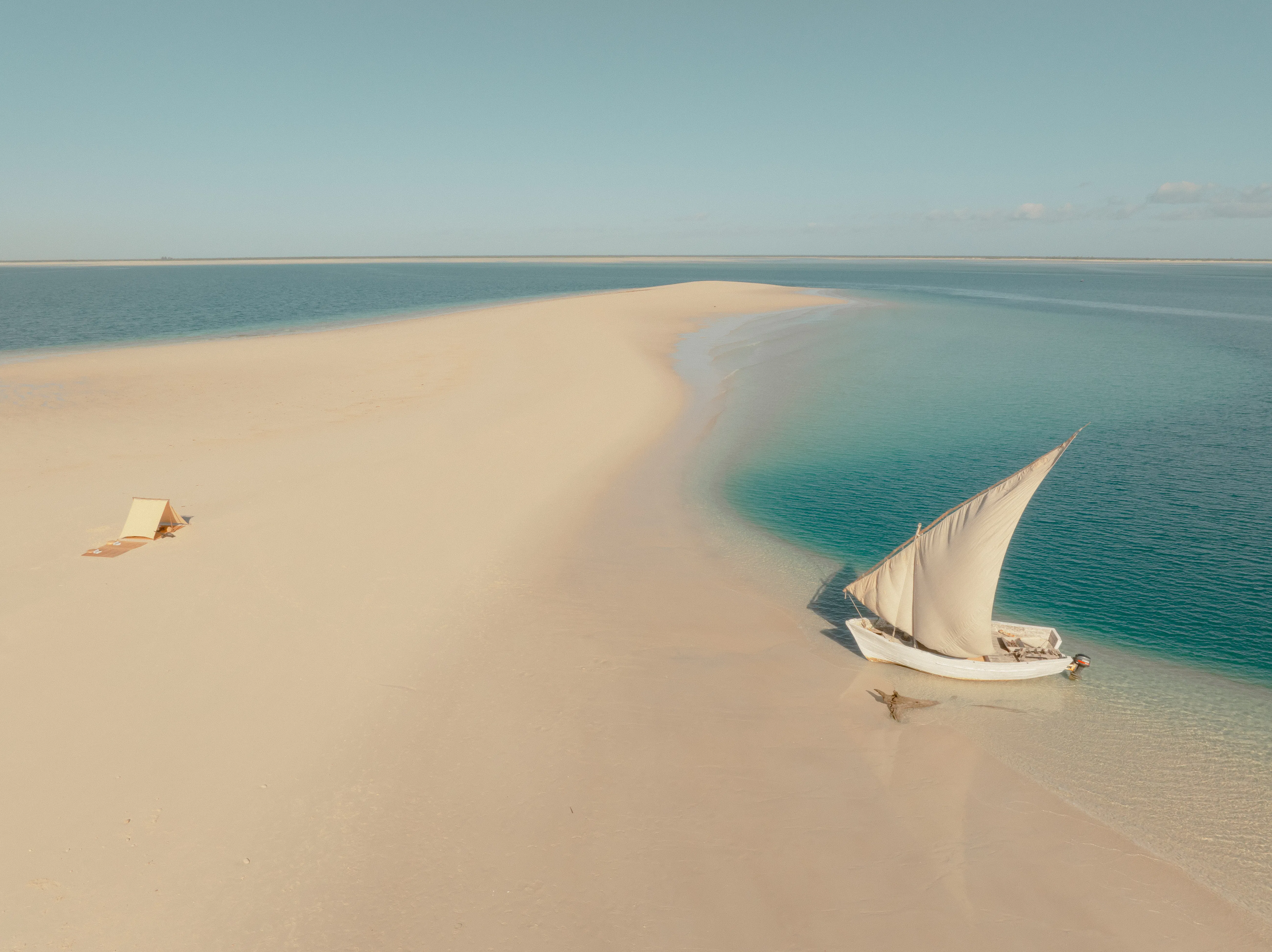 A dhow rests on a curving sandbar in Mozambique, surrounded by pale sand and clear turquoise water below.