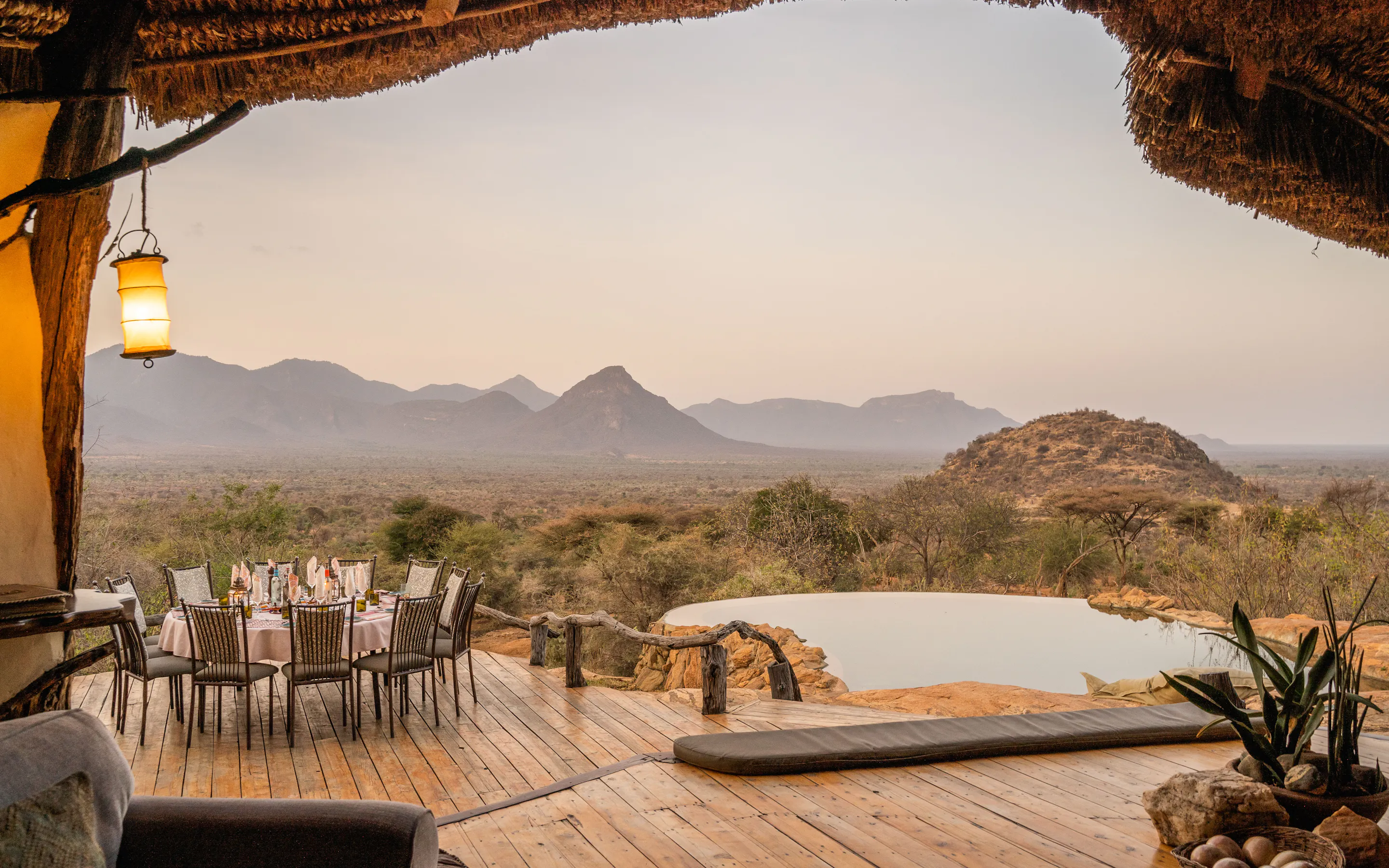 A deck with dining table and plunge pool looks across rocky hills and wide plains at Sarara beneath a pale sky.