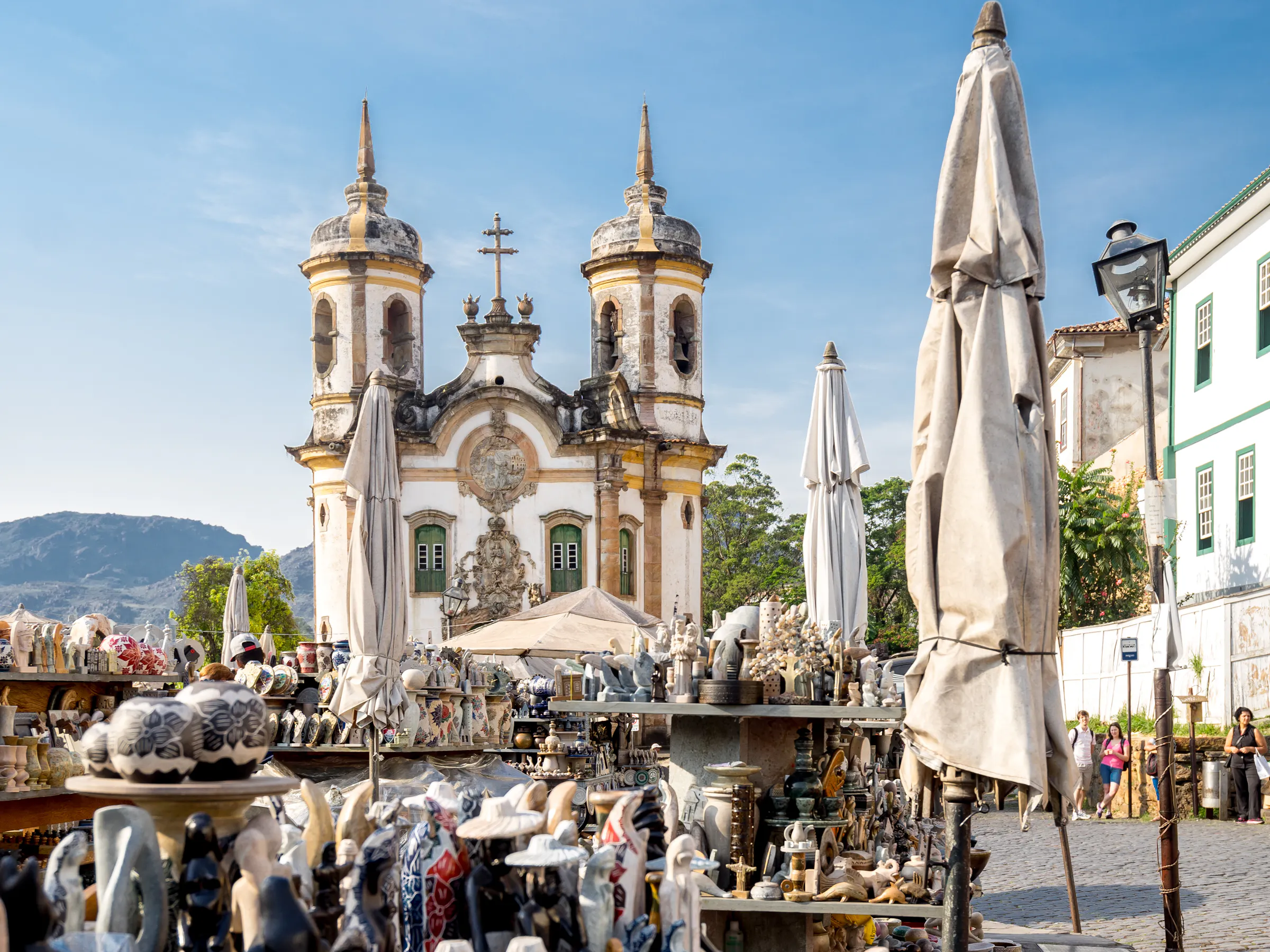 A church rises beyond an artisan market in Ouro Preto, with ceramic stalls and mountains under a clear sky.