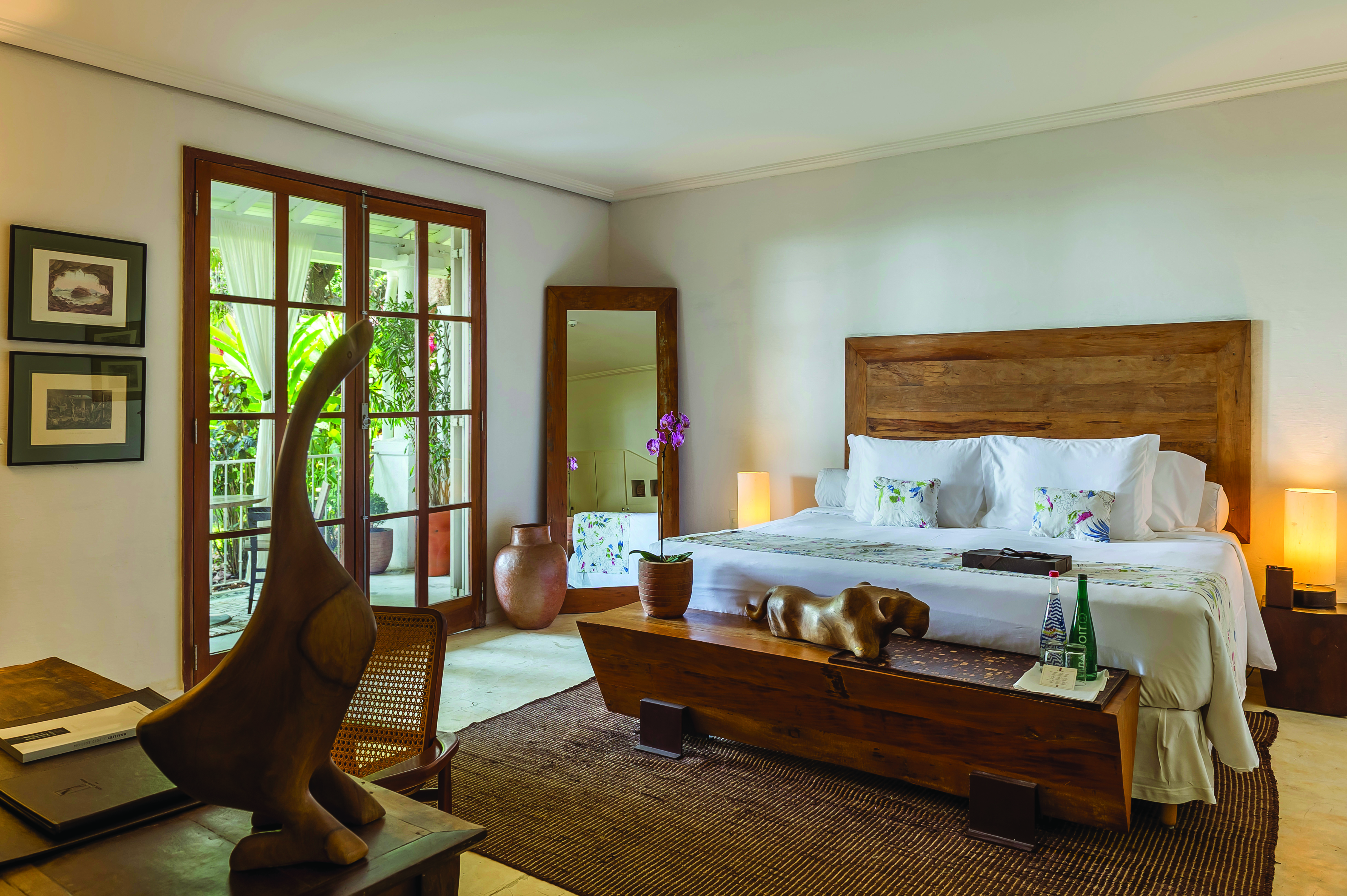 A bright bedroom at Santa Teresa MGallery opens to a leafy balcony, with warm wood furniture and soft light.