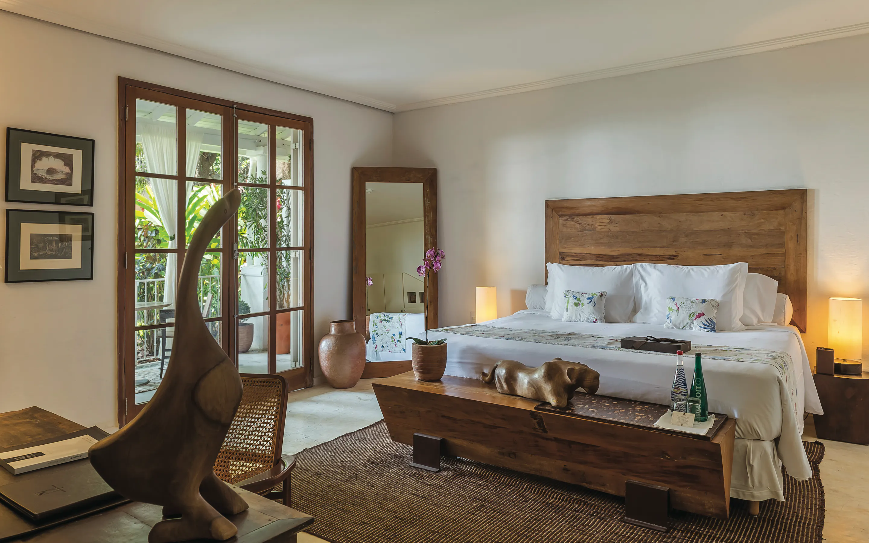 A bright bedroom at Santa Teresa MGallery opens to a leafy balcony, with warm wood furniture and soft light.