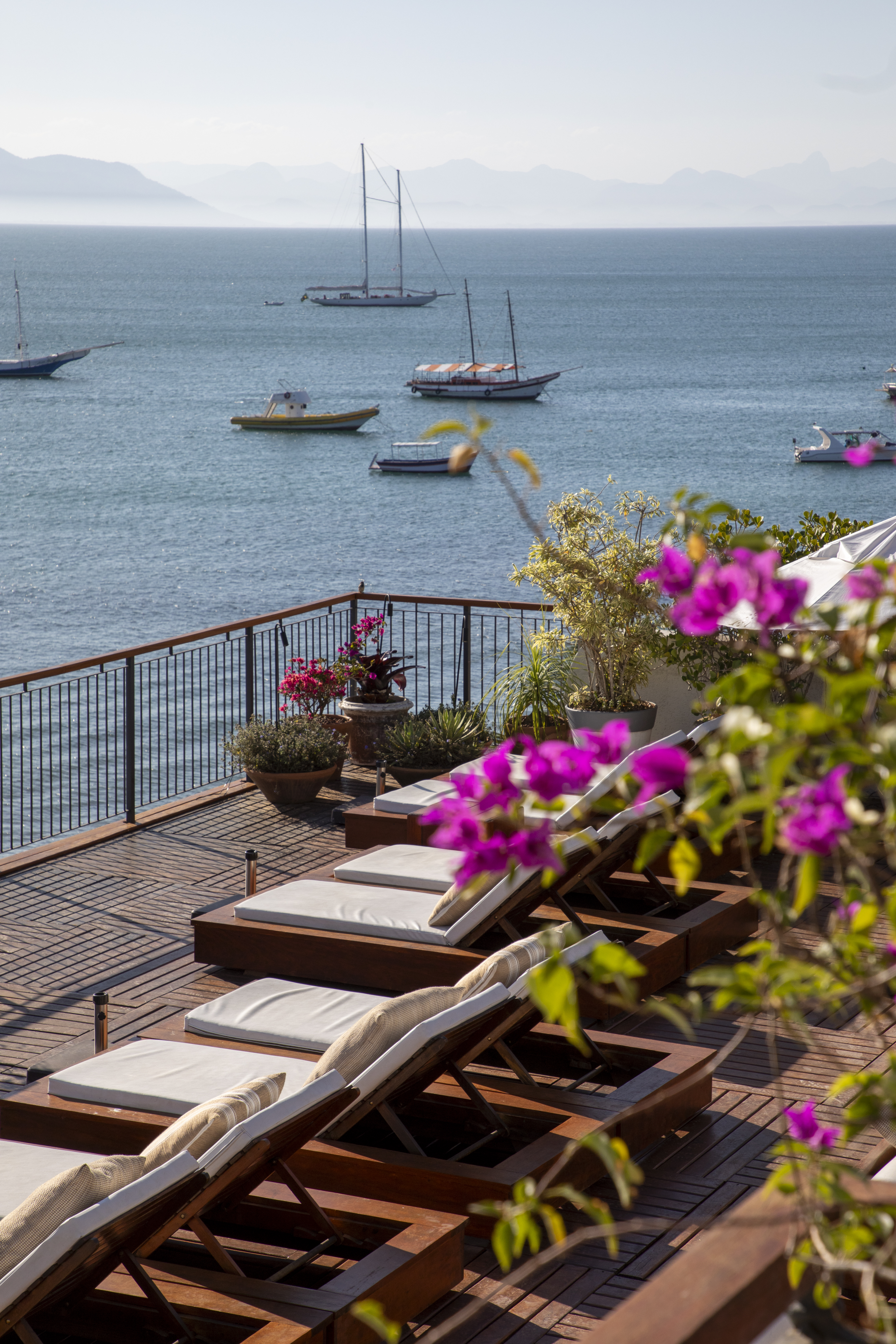 Loungers and flowering planters line a terrace above the bay at Casas Brancas Boutique Hotel in Búzios at sunset.