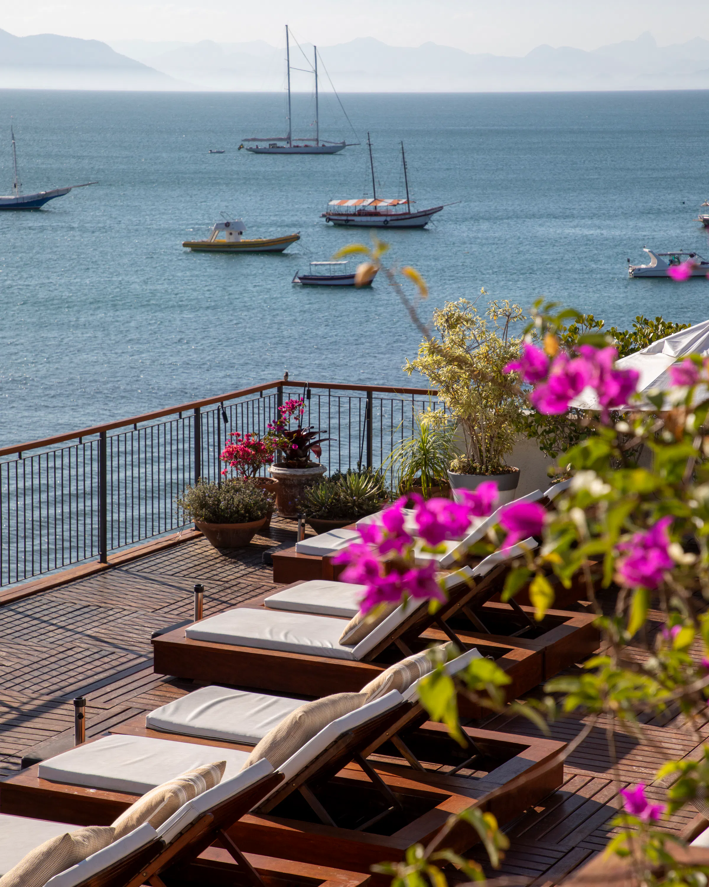 Loungers and flowering planters line a terrace above the bay at Casas Brancas Boutique Hotel in Búzios at sunset.